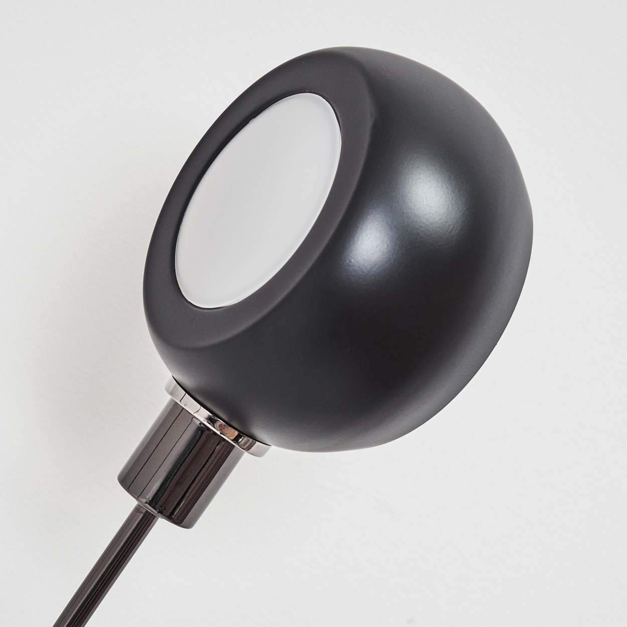 Nahaufnahme einer schwarzen Lampe mit weißem Licht. Die Lampe befindet sich auf weißem Hintergrund. Die Lampe ist zum Betrachter hin abgewinkelt.