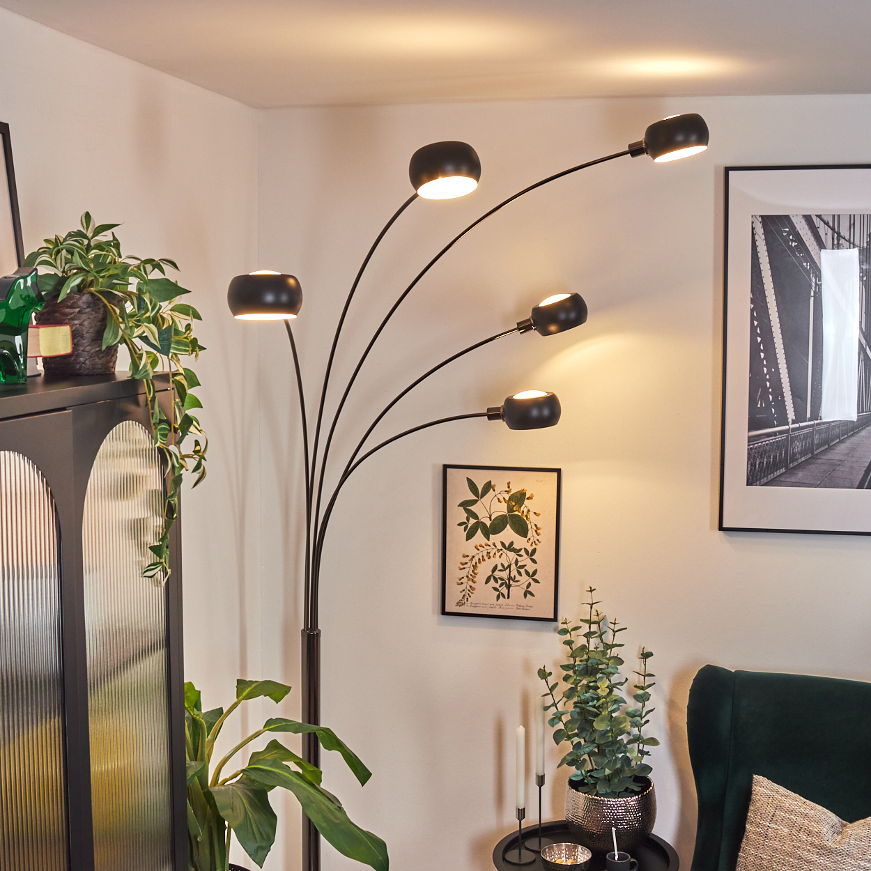 Ein modernes Wohnzimmer mit schwarzer Stehlampe, Pflanzen, einem Gemälde und einem grünen Sessel.