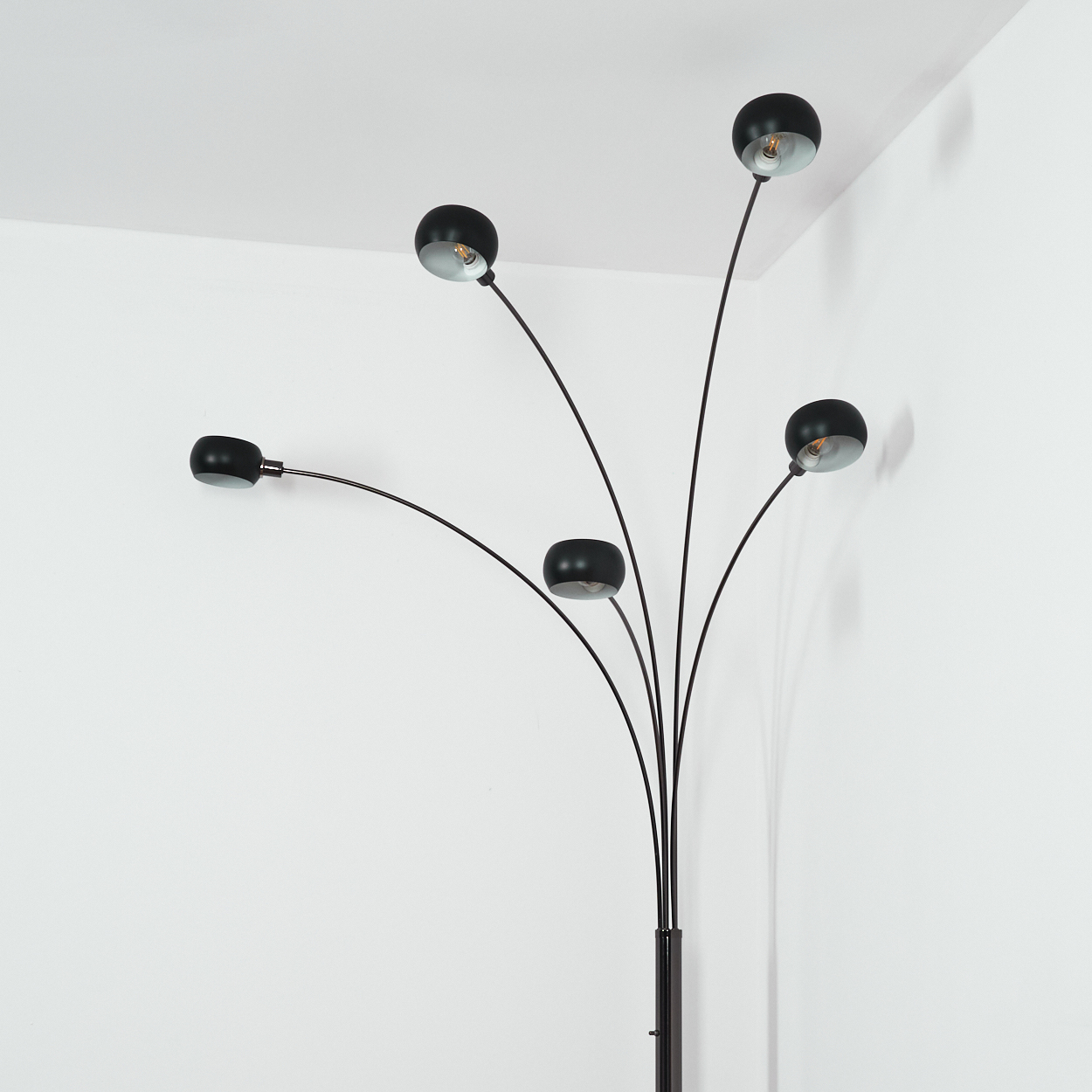 Eine moderne schwarze Stehlampe mit fünf gebogenen Armen, die jeweils einen schwarzen Lampenschirm halten. Der Hintergrund ist eine weiße Wand.