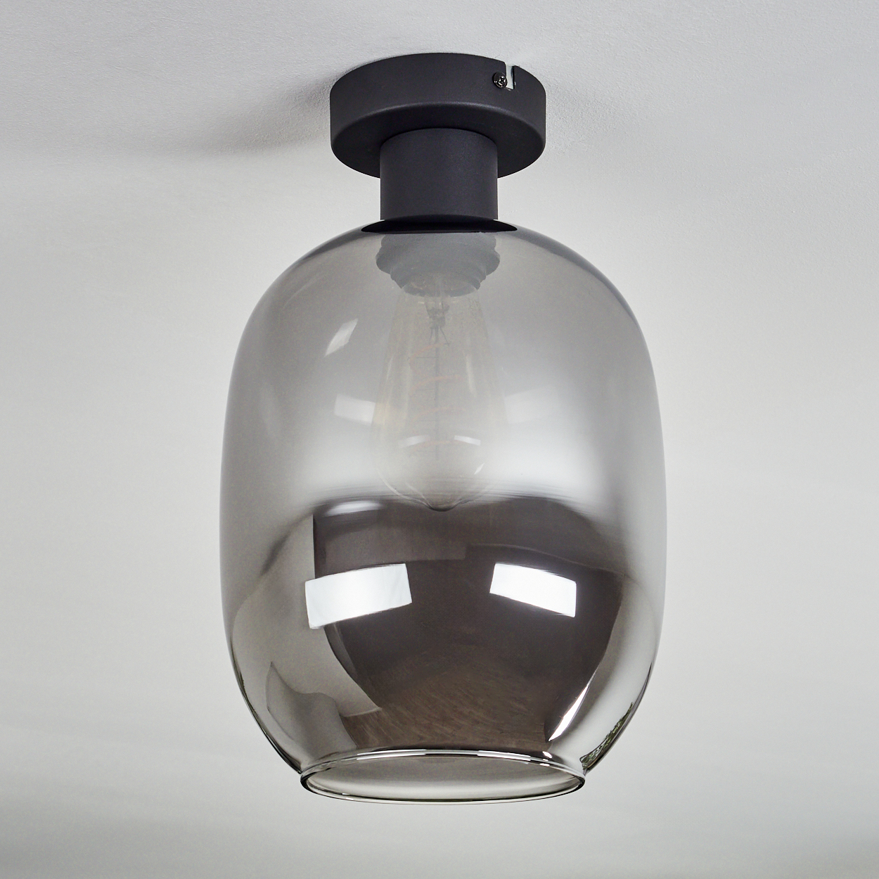 Eine moderne Deckenleuchte mit rauchfarbenem Glasschirm und schwarzer Halterung. Das Licht befindet sich an einer weißen Decke.