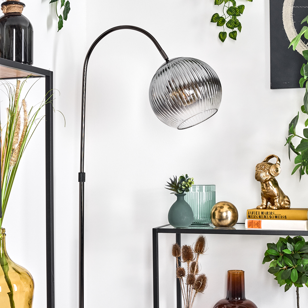 Eine moderne Stehlampe mit Glasschirm, Pflanzen, Vasen und Dekorationsgegenständen auf Regalen sind sichtbar.