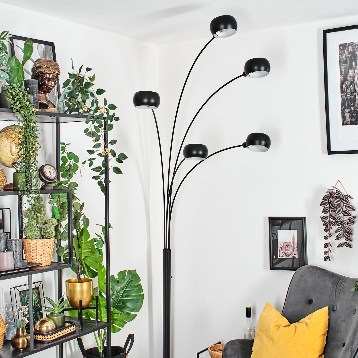 Ein modernes Wohnzimmer mit schwarzer Stehlampe, Regalen mit Pflanzen und einem grauen Sessel mit gelbem Kissen.