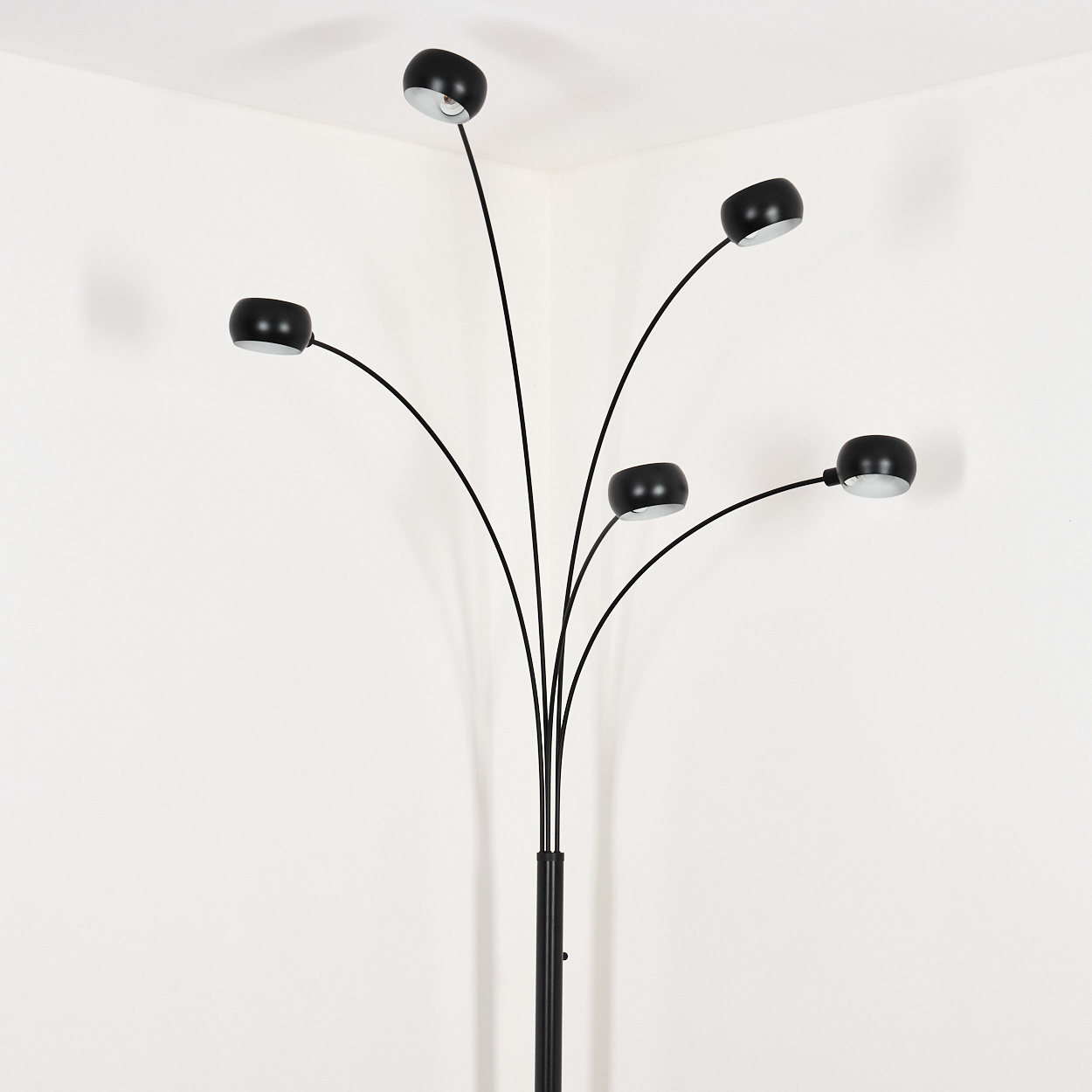 Eine schwarze Bogenlampe mit fünf verstellbaren Köpfen. Sie steht in der Ecke eines weißen Raumes.