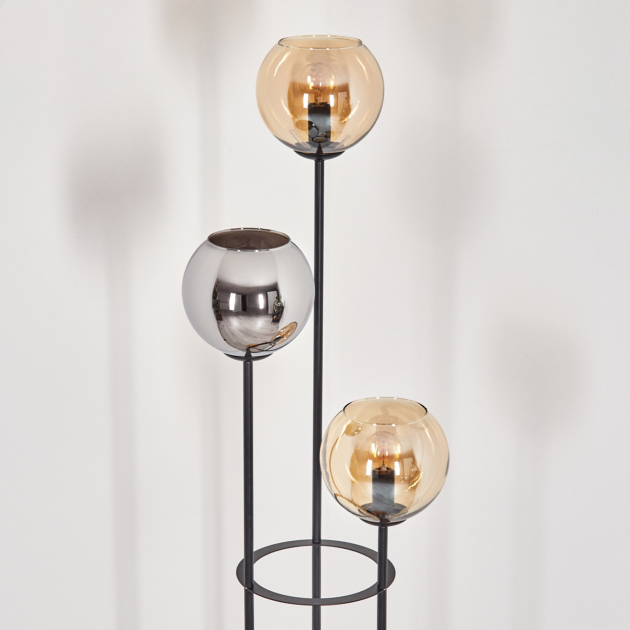 Eine moderne Stehlampe mit drei kugelförmigen Leuchten. Zwei sind bernsteinfarben, eine ist verchromt. Der Sockel und die Tragstruktur sind schwarz.