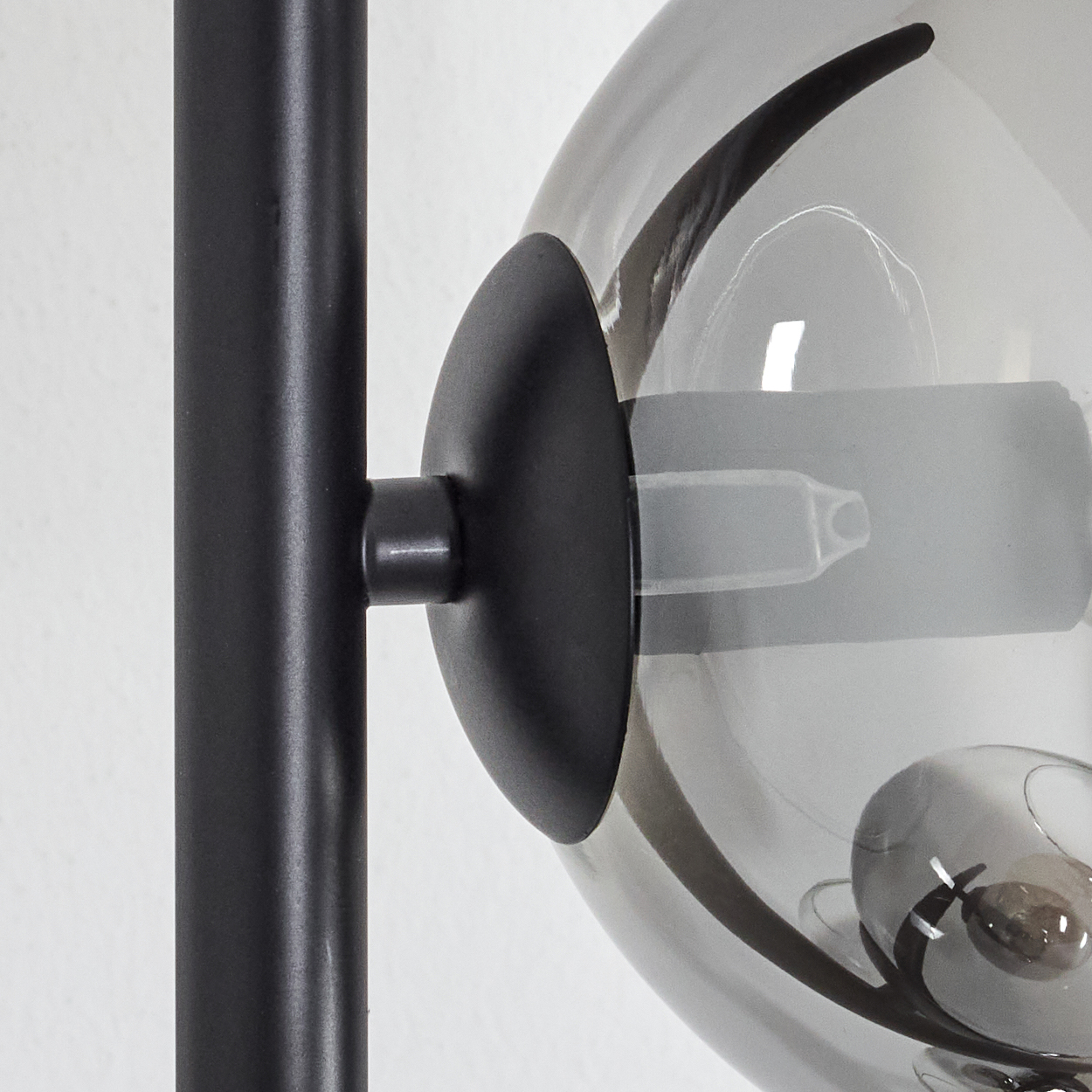 Nahaufnahme einer modernen Lampe. Sie hat einen schwarzen Metallmast und einen kugelförmigen, rauchigen Glasschirm mit einer Glühbirne.