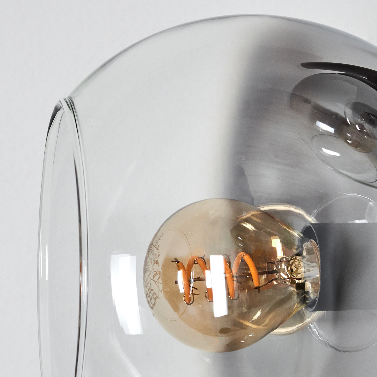 Nahaufnahme einer Leuchte mit klarem Glasschirm. Eine große, warmtonige Glühbirne ist im Schirm zu sehen.