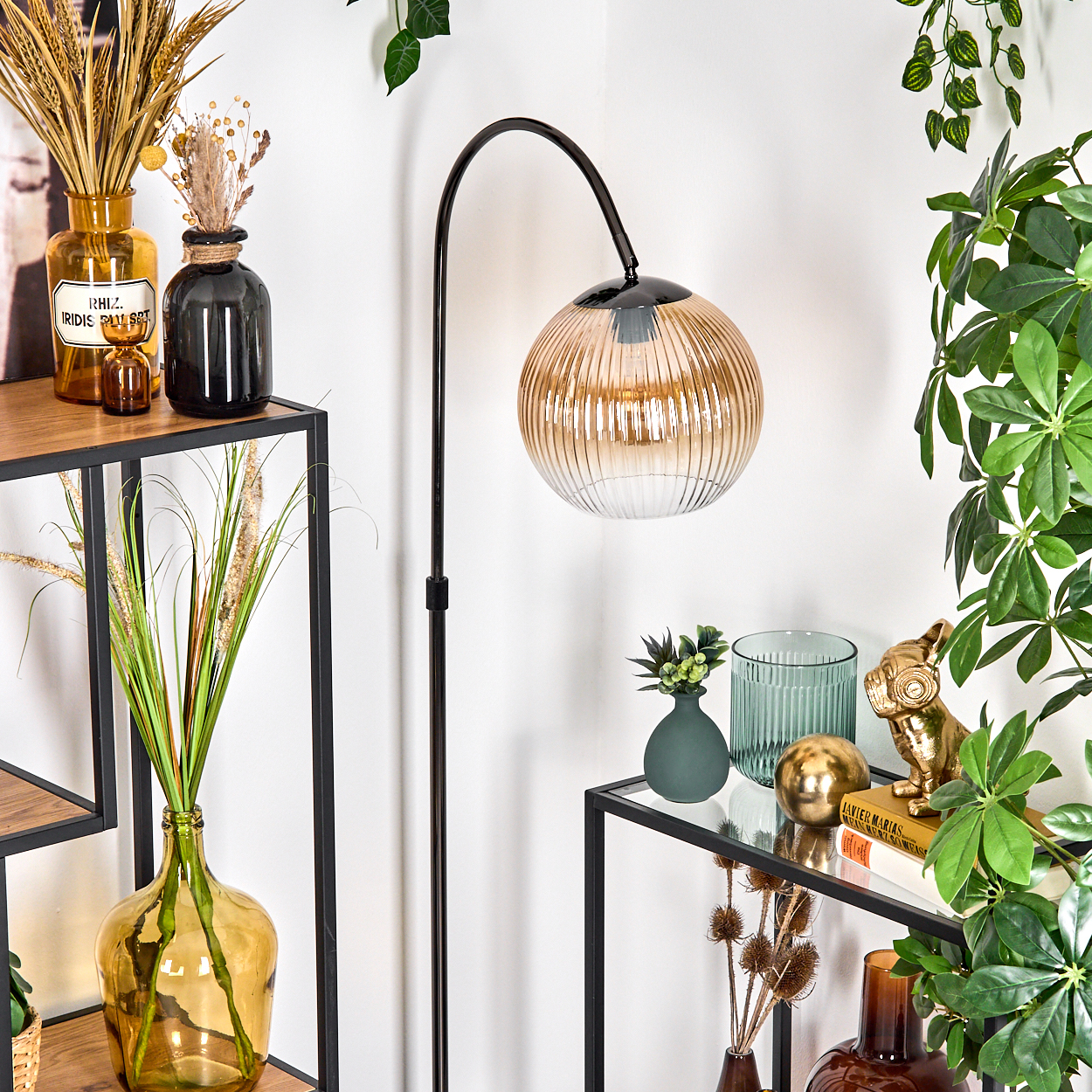 Eine Zimmerecke mit Stehlampe und Glasregalen mit Dekorationsartikeln, Pflanzen und Vasen.