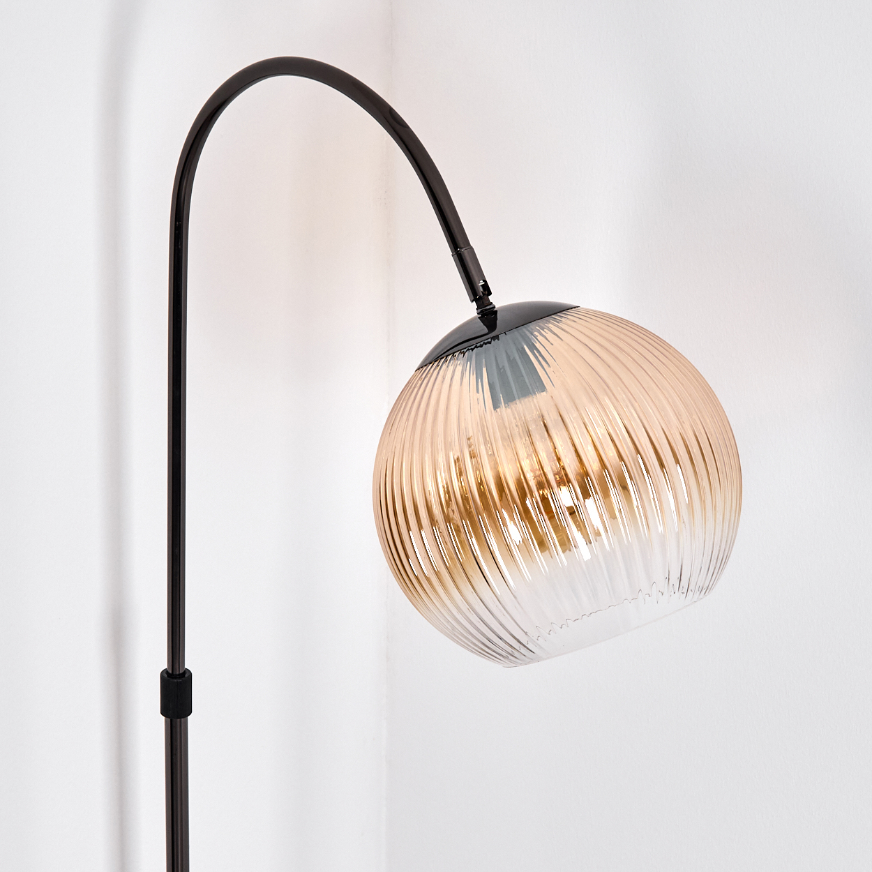 Eine moderne Stehlampe mit gebogenem schwarzem Stiel und einem kugelförmigen, gerippten Glasschirm in Bernstein- und Klartönen.