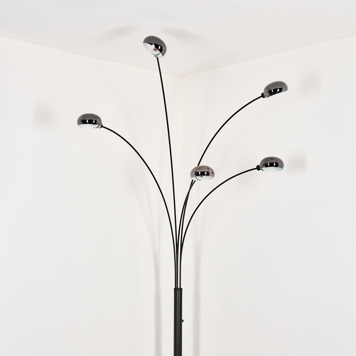 Eine moderne schwarze Stehlampe mit fünf verchromten Kuppellampen. Sie steht in einer weißen Ecke und wirft weiche Schatten.
