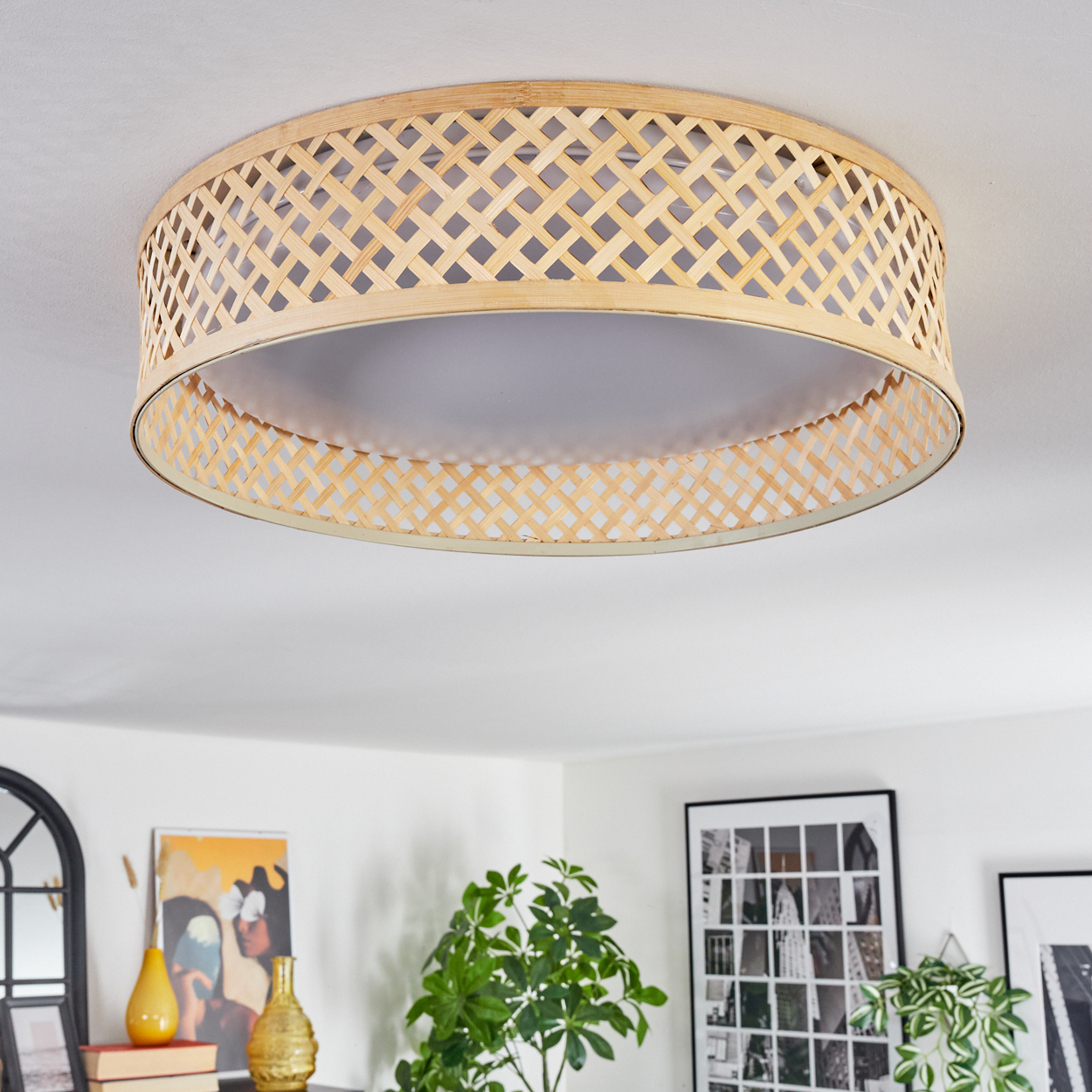 Eine Deckenlampe aus geflochtenem Bambus hängt in einem Raum. Darunter dekorieren Kunst, Pflanzen und Vasen den Raum.