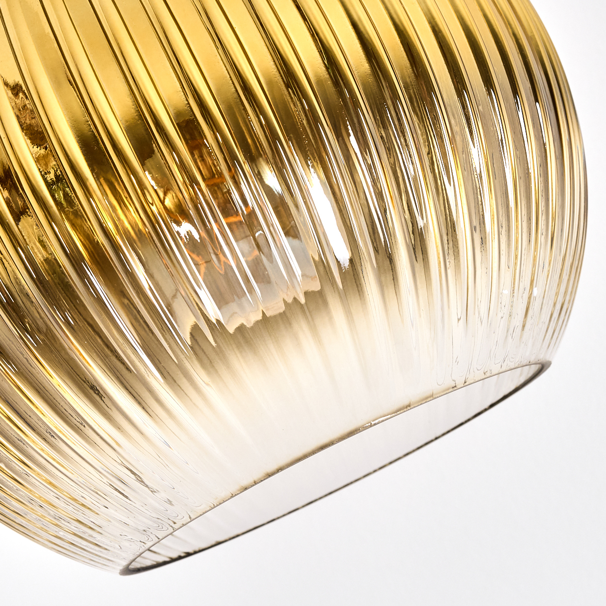 Nahaufnahme eines goldenen, gerippten Glaslampenschirms. Die Glühbirne ist sichtbar. Der Hintergrund ist weiß.