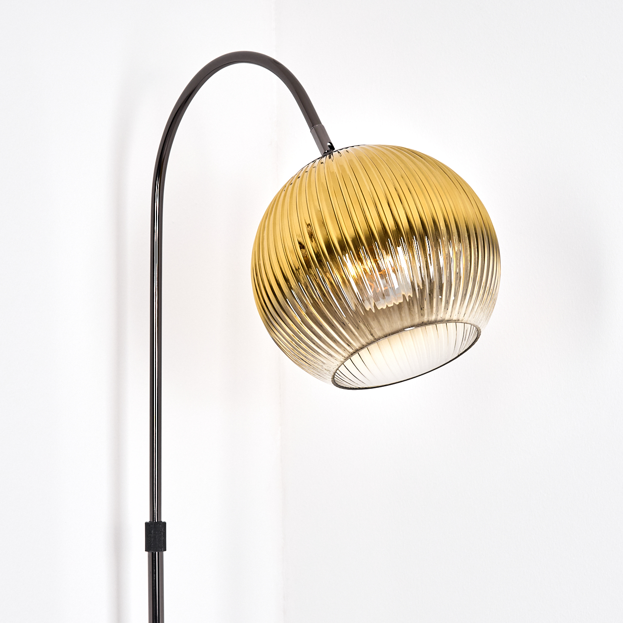 Eine moderne Stehlampe mit goldfarbenem, geripptem Glasschirm. Der schwarze, gebogene Arm erstreckt sich von einem schwarzen Pfahl.
