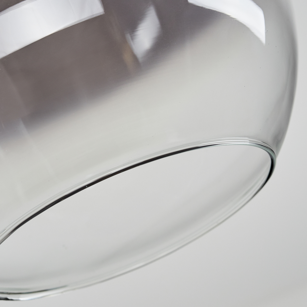 Nahaufnahme eines durchsichtigen Glasschirms. Das Glas wölbt sich nach unten und zeigt Reflexionen. Der Hintergrund ist hellgrau.