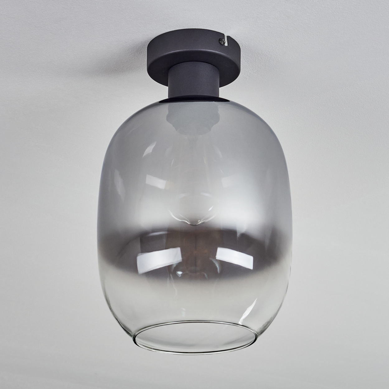 Moderne Deckenlampe mit grauem Glasschirm. Der Schirm hat eine runde Form und ist an einer dunklen Metallbasis an der weißen Decke befestigt.