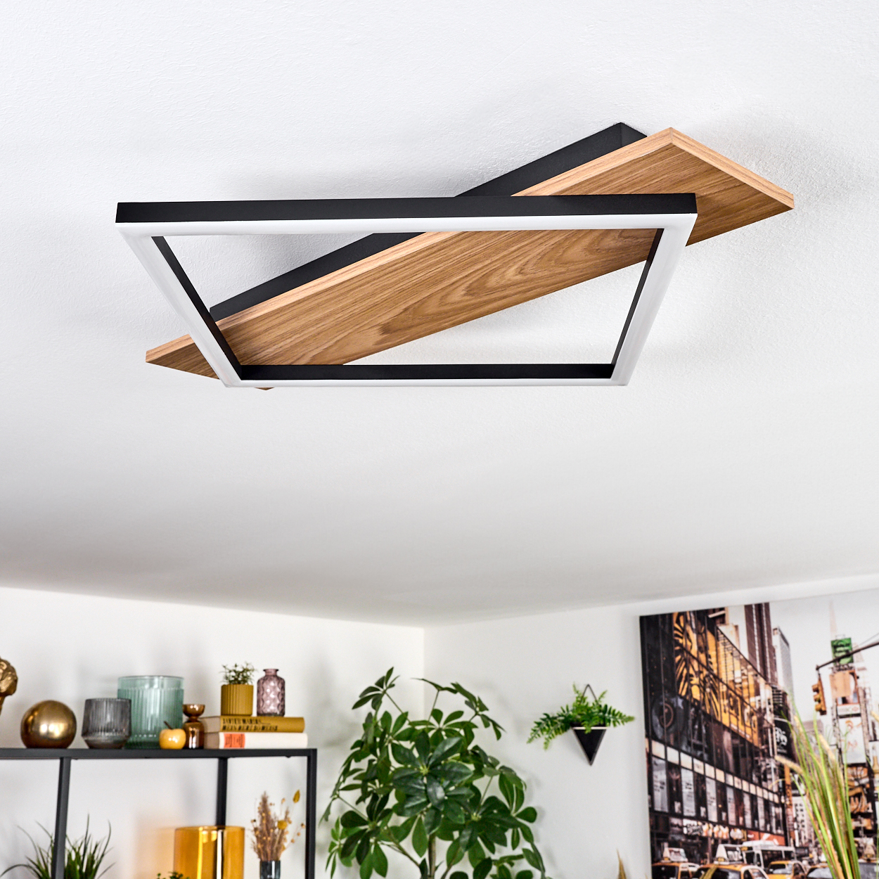 Eine moderne Deckenlampe mit Holz- und schwarzem Rahmen ist installiert. Darunter sind ein Regal mit Dekorationen und eine Pflanze zu sehen.