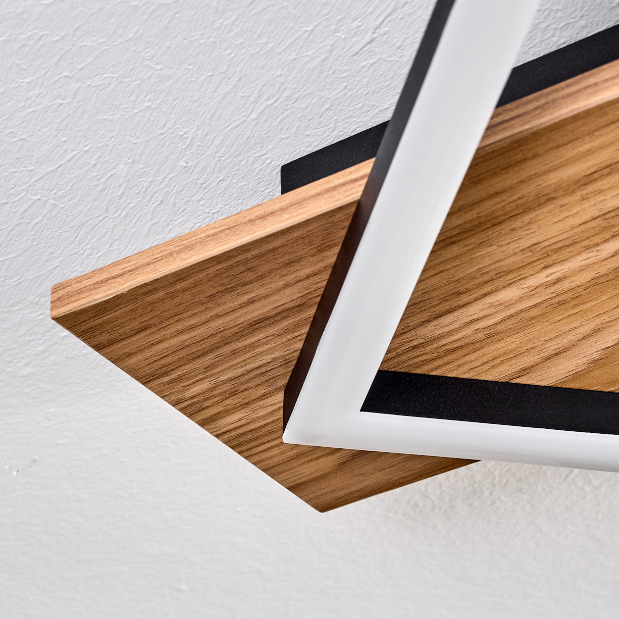 Nahaufnahme eines Holzregals mit weißem und schwarzem geometrischen Design. Der Hintergrund ist eine strukturierte weiße Wand.