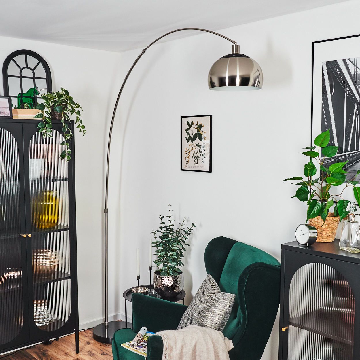 Modernes Wohnzimmer mit grünem Sessel, Stehlampe, Pflanzen und schwarzem Schrank. Kunstwerk und Spiegel an der Wand.