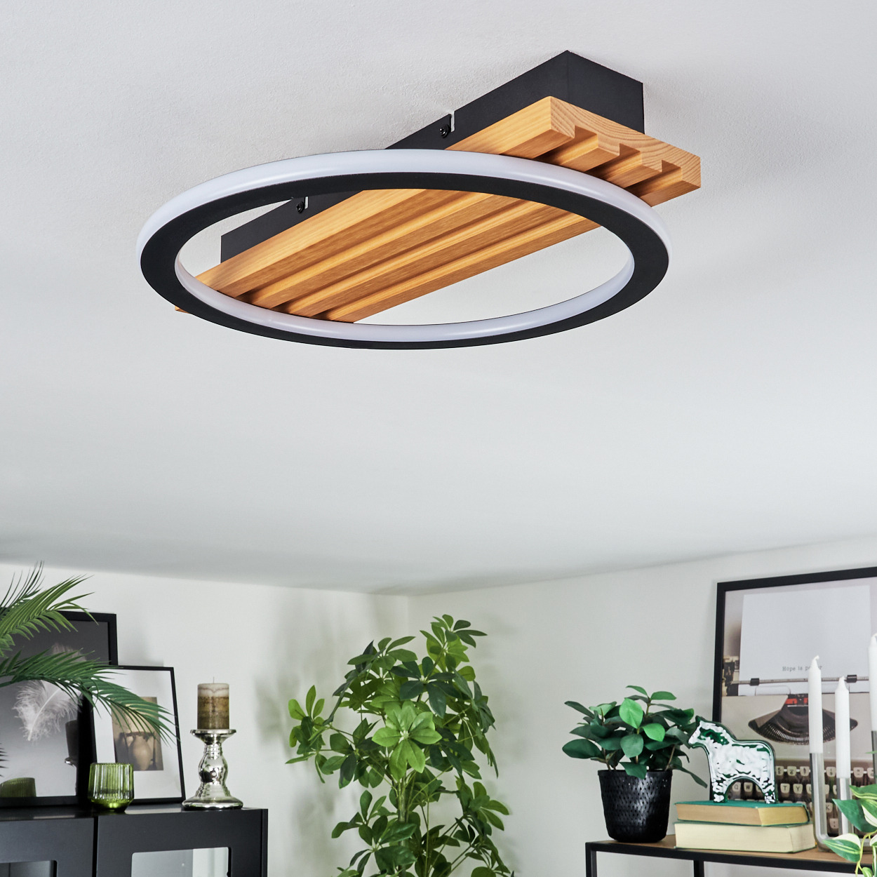 Moderne Deckenleuchte mit Holz- und schwarzem Rahmen, kreisförmigem Licht. Dekorative Pflanzen und gerahmte Bilder im Raum.