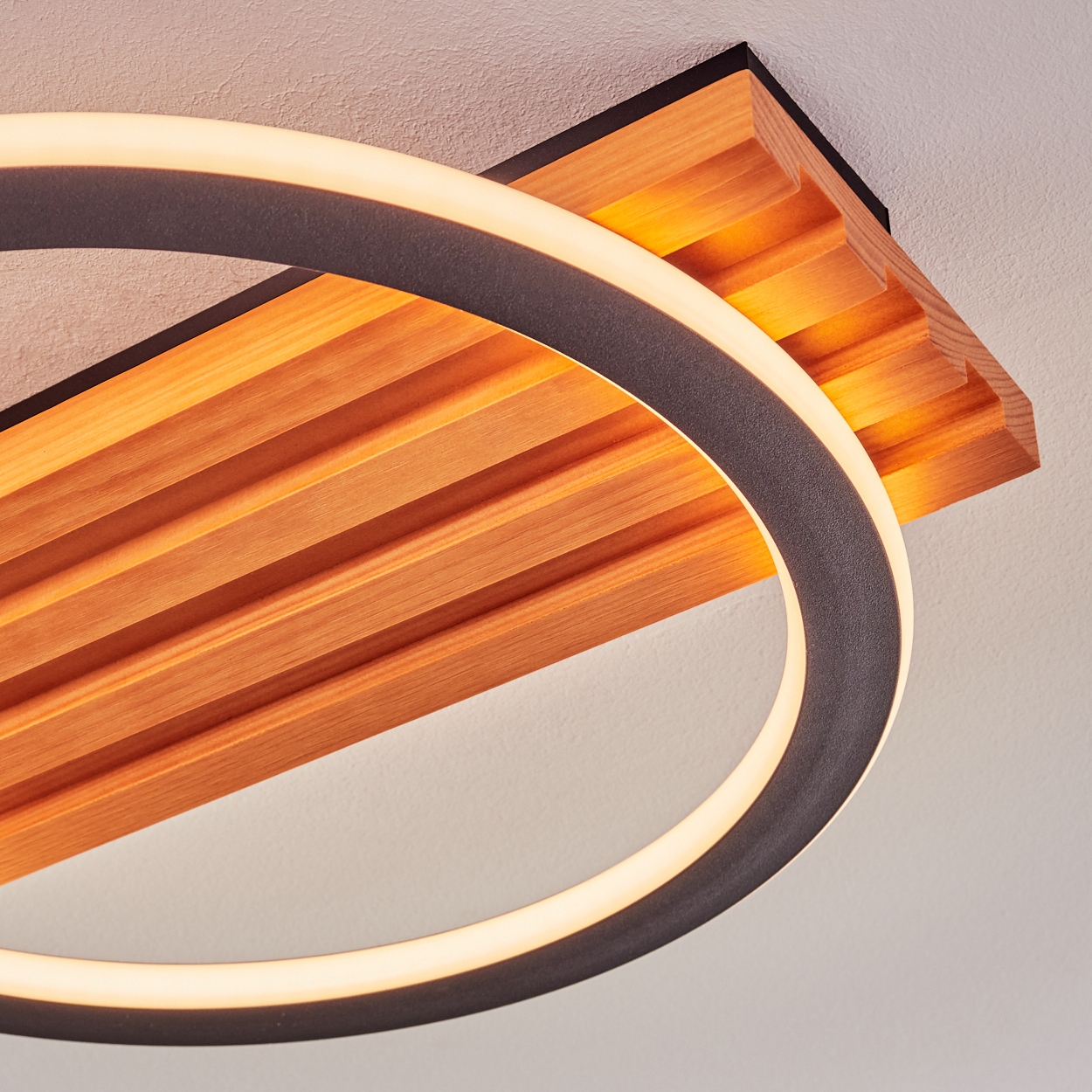 Moderne Deckenleuchte. Sie hat ein kreisförmiges Licht und eine Holzplatte mit parallelen Rillen. Der Hintergrund ist eine weiße Decke.