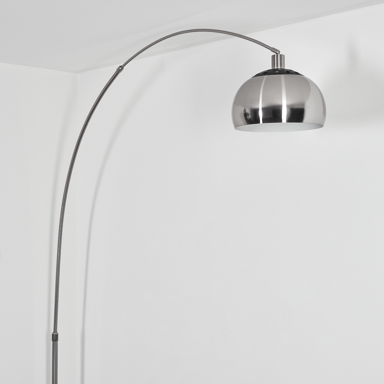 Eine moderne silberne Bogenstehlampe mit einem kuppelförmigen Schirm. Sie steht vor einer weißen Wand in einer Ecke, einfach und elegant.