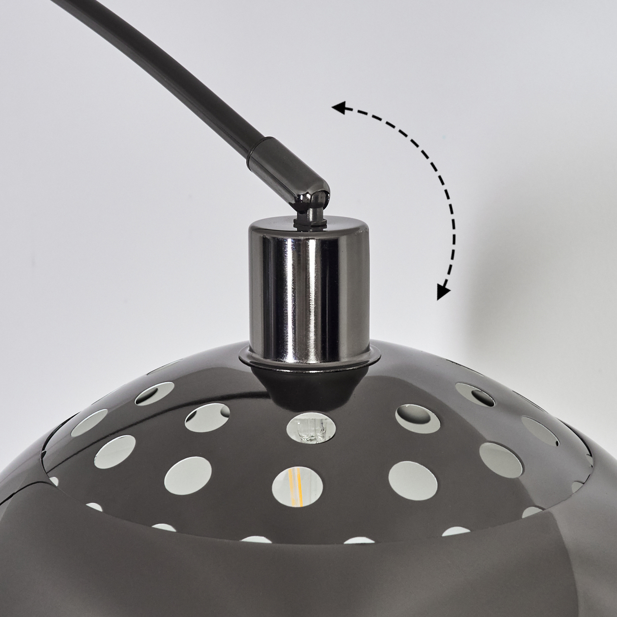 Nahaufnahme einer schwarzen Lampe mit perforiertem Lampenschirm. Ein schwarzer Arm erstreckt sich von oben. Die Lampe steht vor weißem Hintergrund.