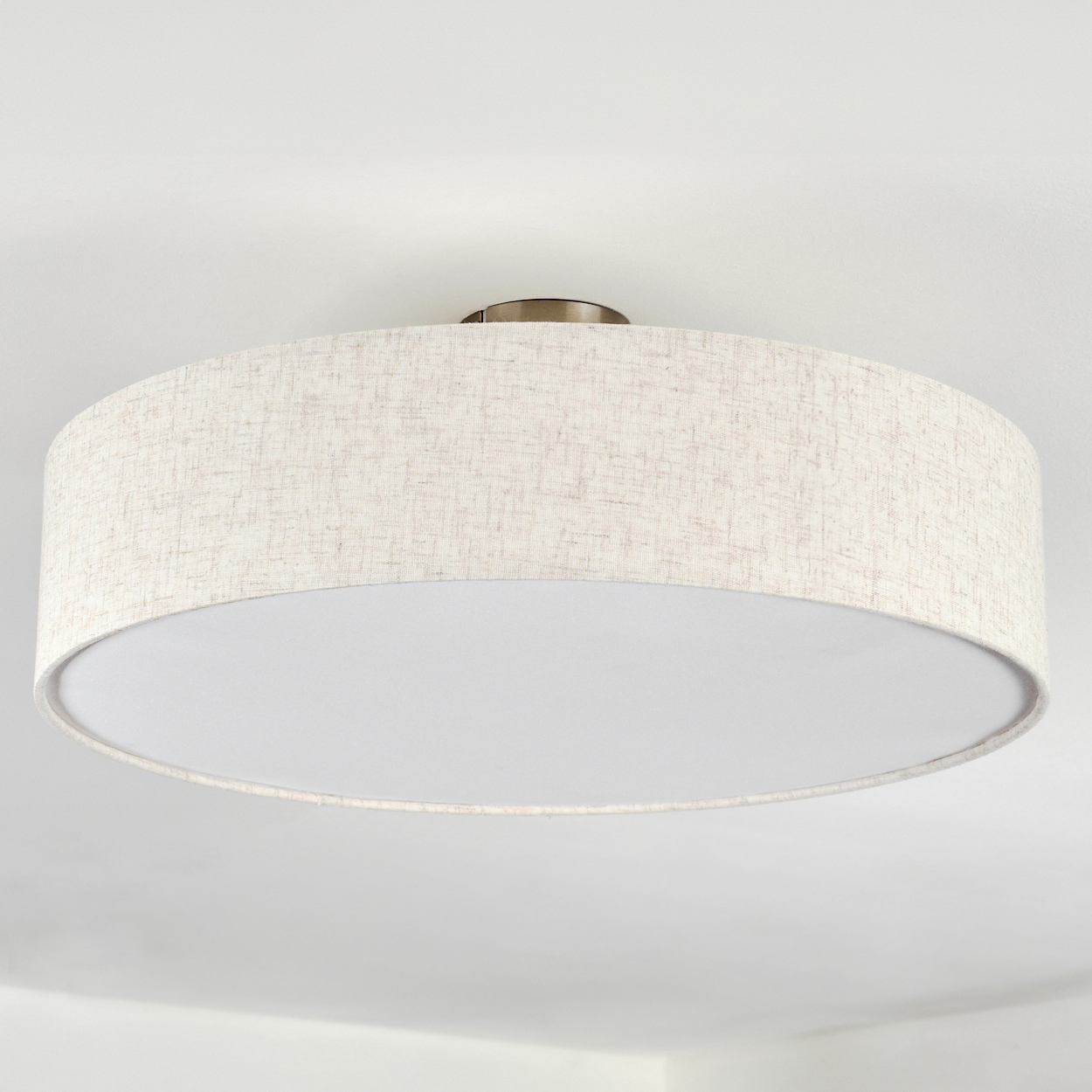 Eine beige trommelförmige Deckenleuchte. Sie hat einen Stoffschirm und ein weißes Innere, das an einer weißen Decke befestigt ist.
