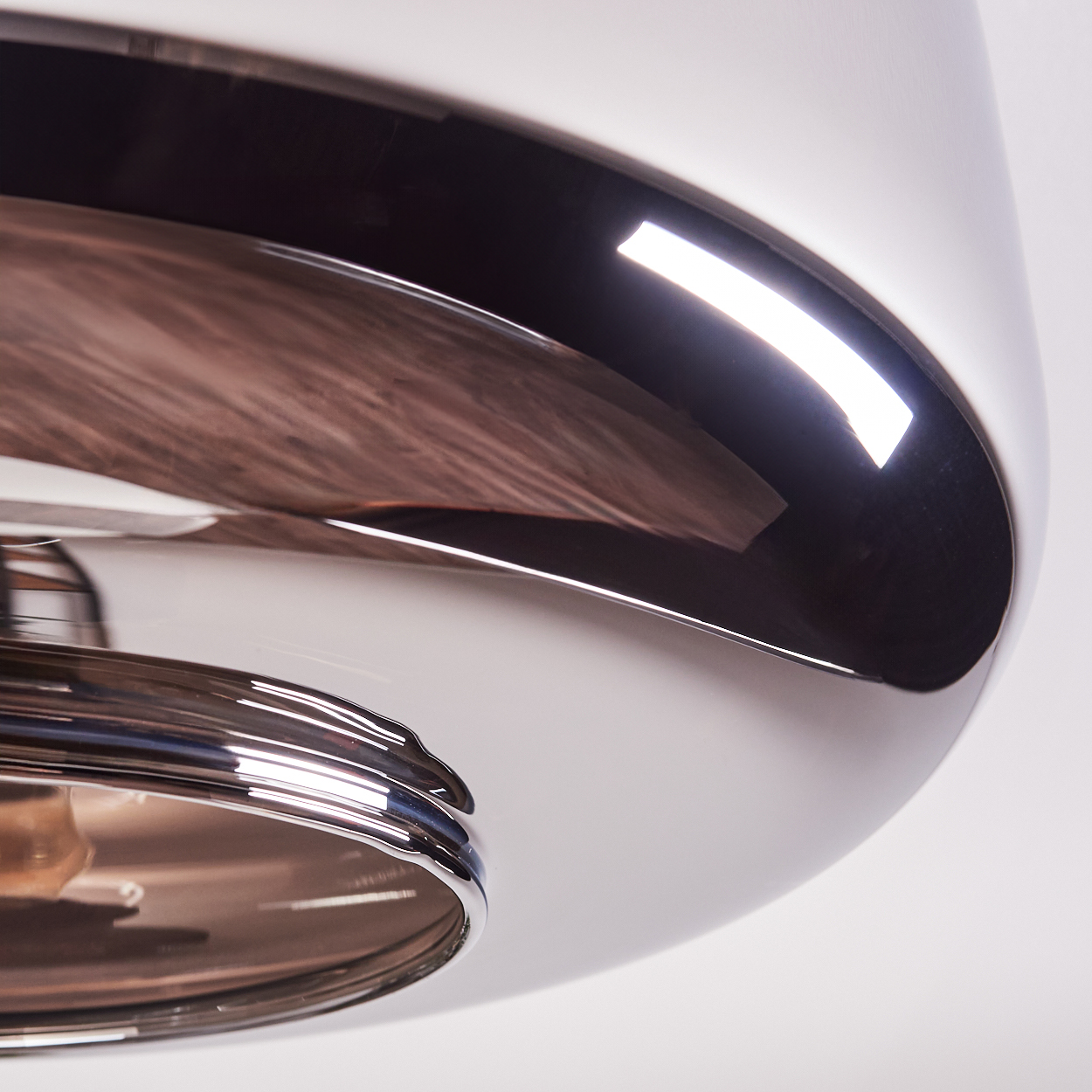 Nahaufnahme einer glänzenden Metallleuchte. Das Design weist eine geschwungene, reflektierende Oberfläche mit dunklem Innenraum und hellem Licht auf.