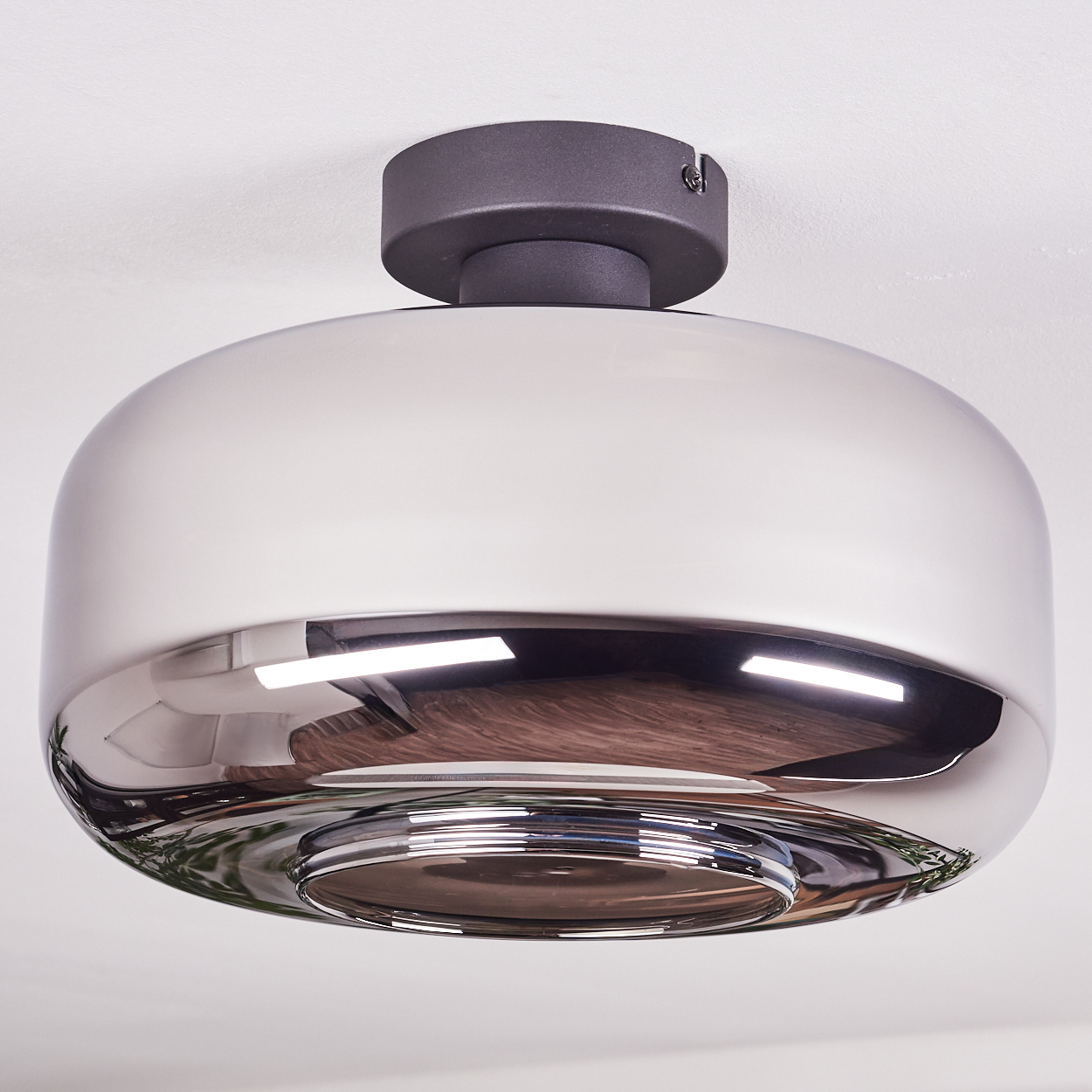 Eine moderne Deckenlampe mit silbernem, reflektierendem Schirm und dunkelgrauem Sockel, montiert an einer weißen Decke.