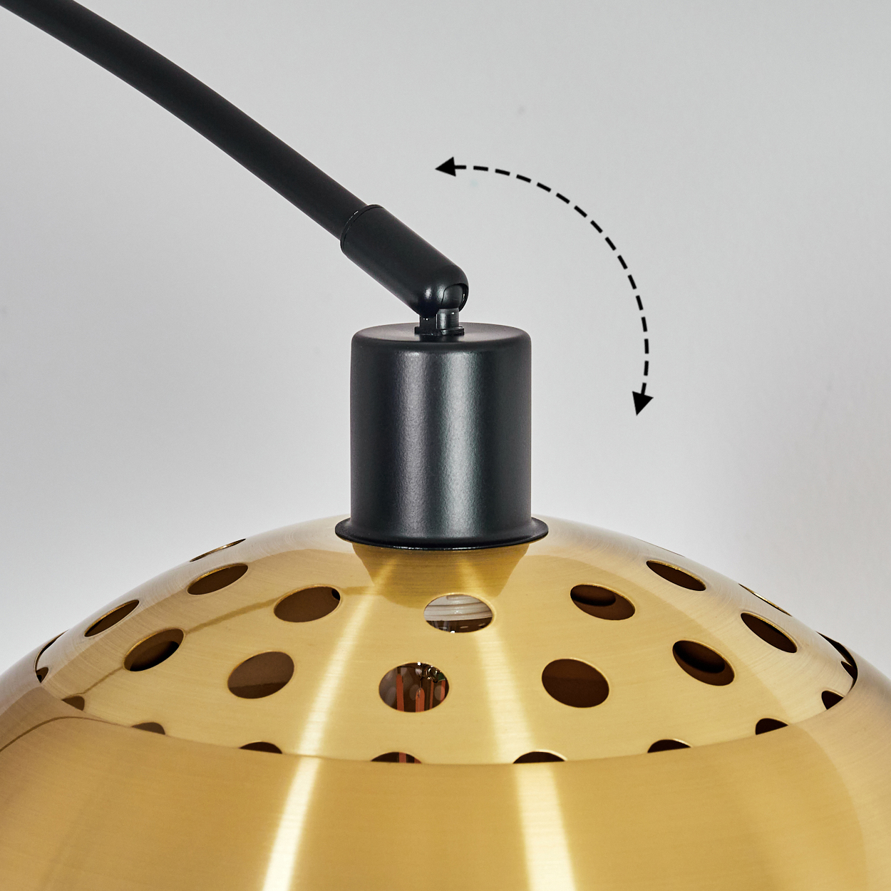 Nahaufnahme einer Lampe. Schwarzer Arm und Sockel tragen einen goldfarbenen, perforierten Schirm. Pfeil zeigt Bewegung. Weißer Hintergrund.