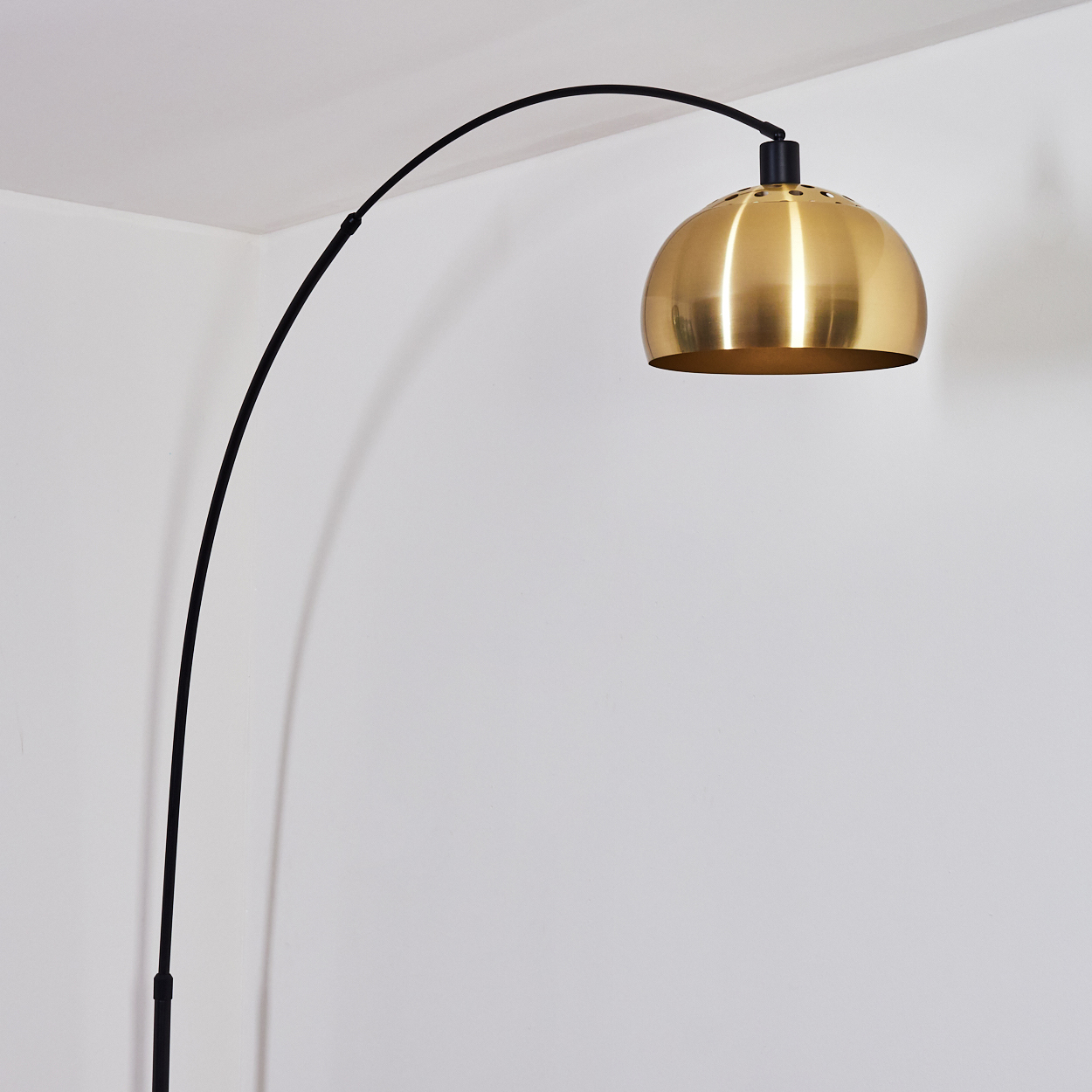 Eine moderne Bogenlampe mit goldenem Lampenschirm. Die Lampe ist schwarz, mit einem gebogenen Arm. Weiße Wand im Hintergrund.