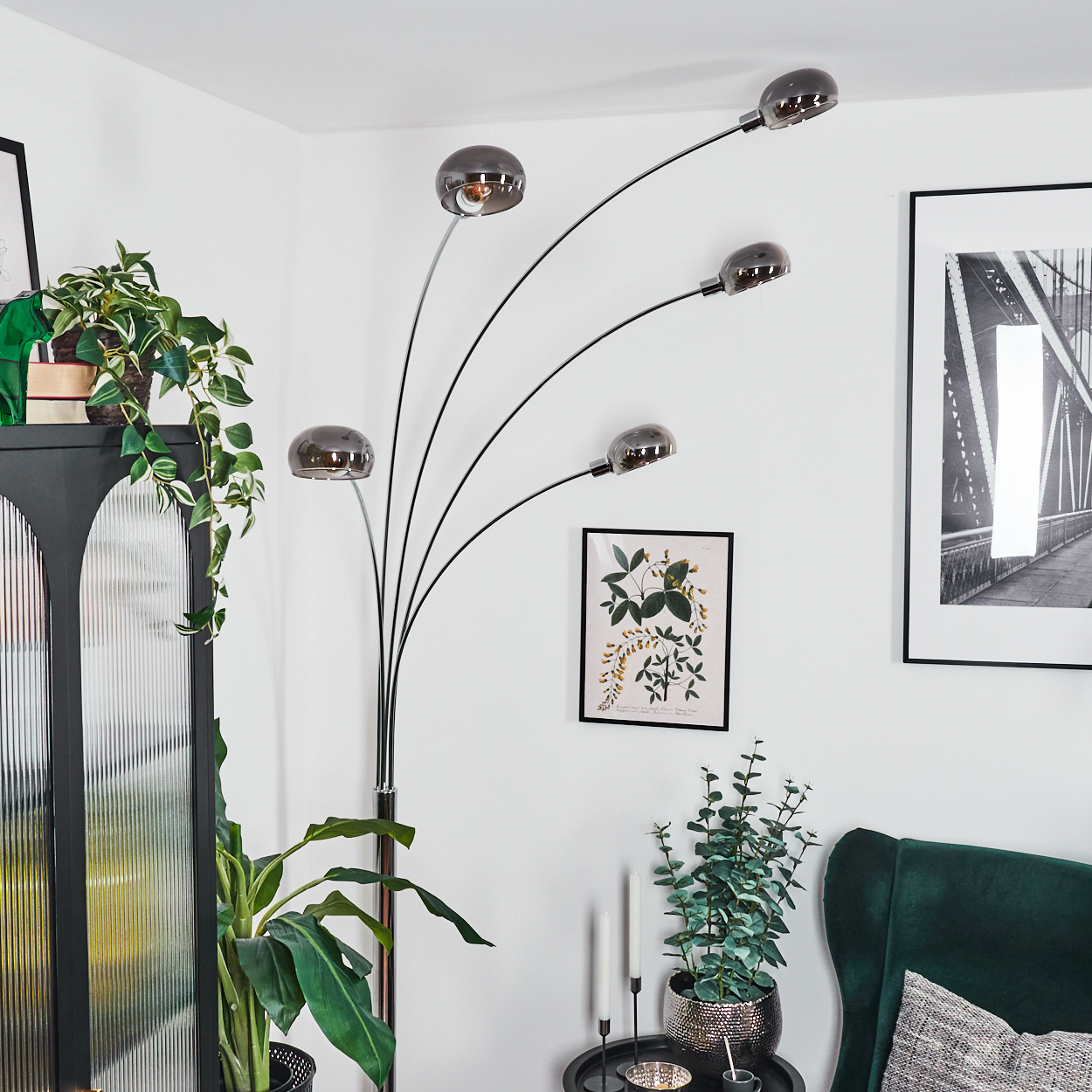 Ein modernes Wohnzimmer mit einer einzigartigen Lampe, Pflanzen und gerahmter Kunst. Die Lampe hat fünf Lichter. Ein grüner Sessel steht in der Ecke.