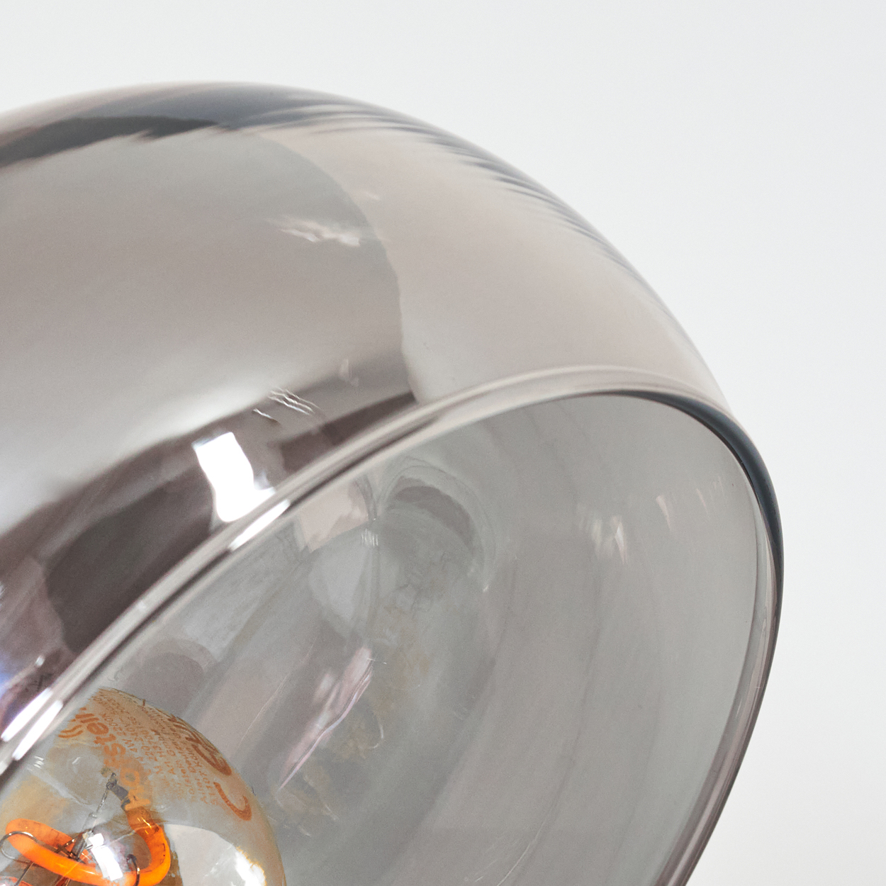 Nahaufnahme eines Glasschirmes mit Glühbirne. Der Schirm reflektiert, fängt Licht ein. Weißer Hintergrund.