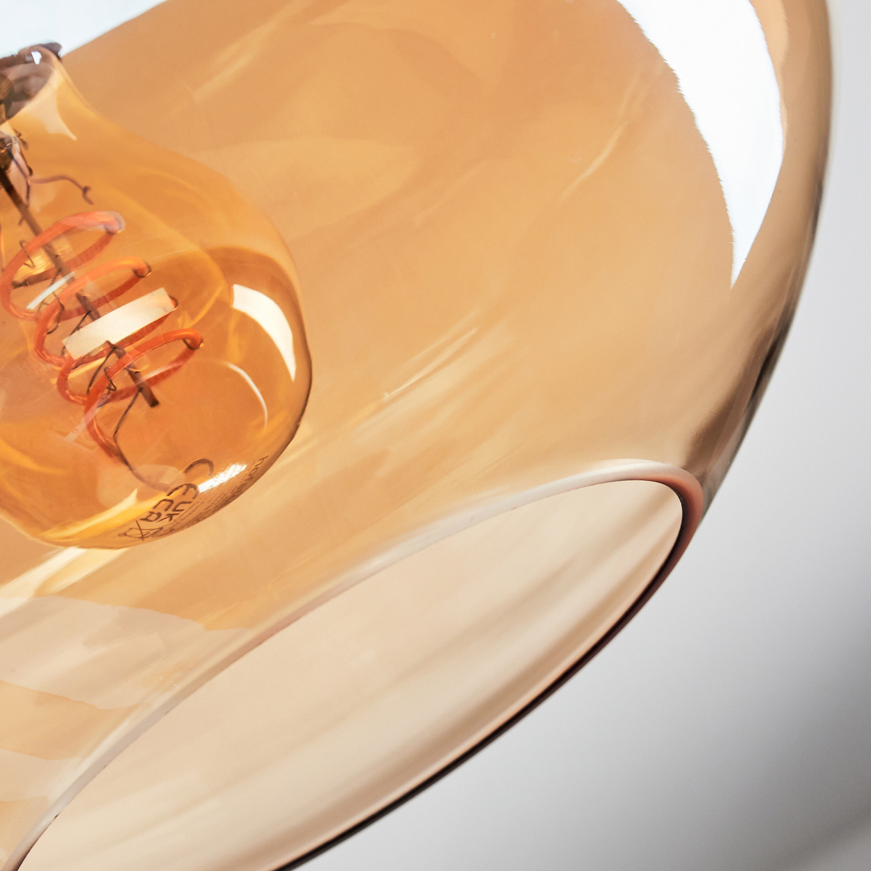 Nahaufnahme einer Leuchte. Ein klarer Glasschirm über einer Glühbirne mit sichtbarem orangefarbenem Glühfaden. Weißer Hintergrund.