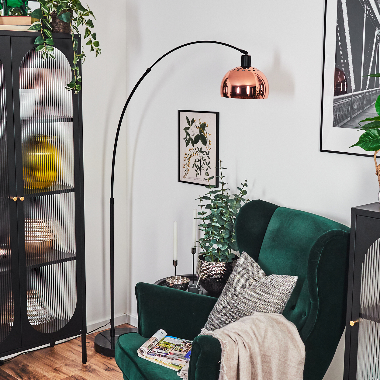 Ein Zimmer mit grünem Samtsessel, Kupferlampe, schwarzem Schrank und botanischem Druck an der Wand.