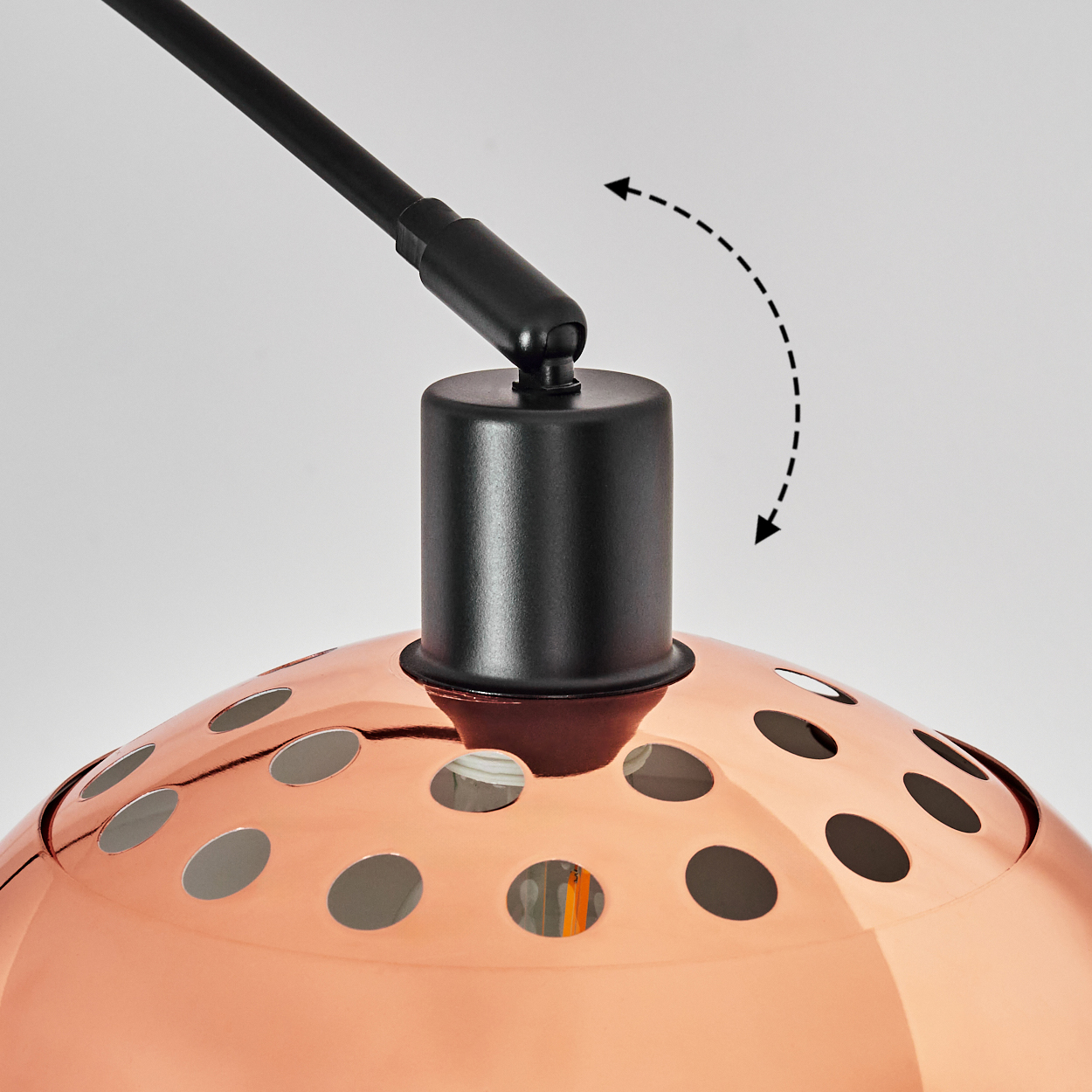 Nahaufnahme einer Kupferlampe mit schwarzem Arm. Die Lampe hat einen perforierten Schirm und einen schwarzen zylindrischen Sockel. Ein Pfeil zeigt die Verstellbarkeit.