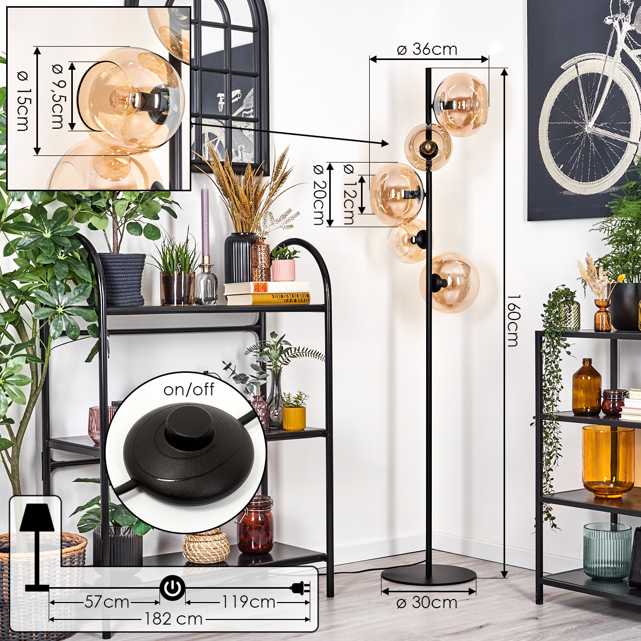 Eine moderne Stehlampe mit kugelförmigen Schirmen, schwarzem Rahmen und Fußschalter. Regale mit Pflanzen, Dekoration und Fahrradkunst sind sichtbar.