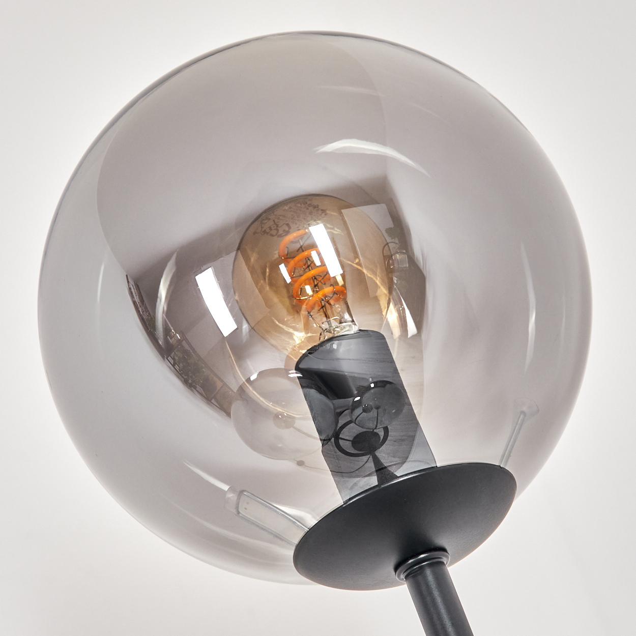 Nahaufnahme einer modernen Lampe. Eine klare Glaskugel umgibt eine Glühbirne mit einem orangefarbenen Glühfaden. Der Sockel ist schwarz und der Hintergrund ist weiß.