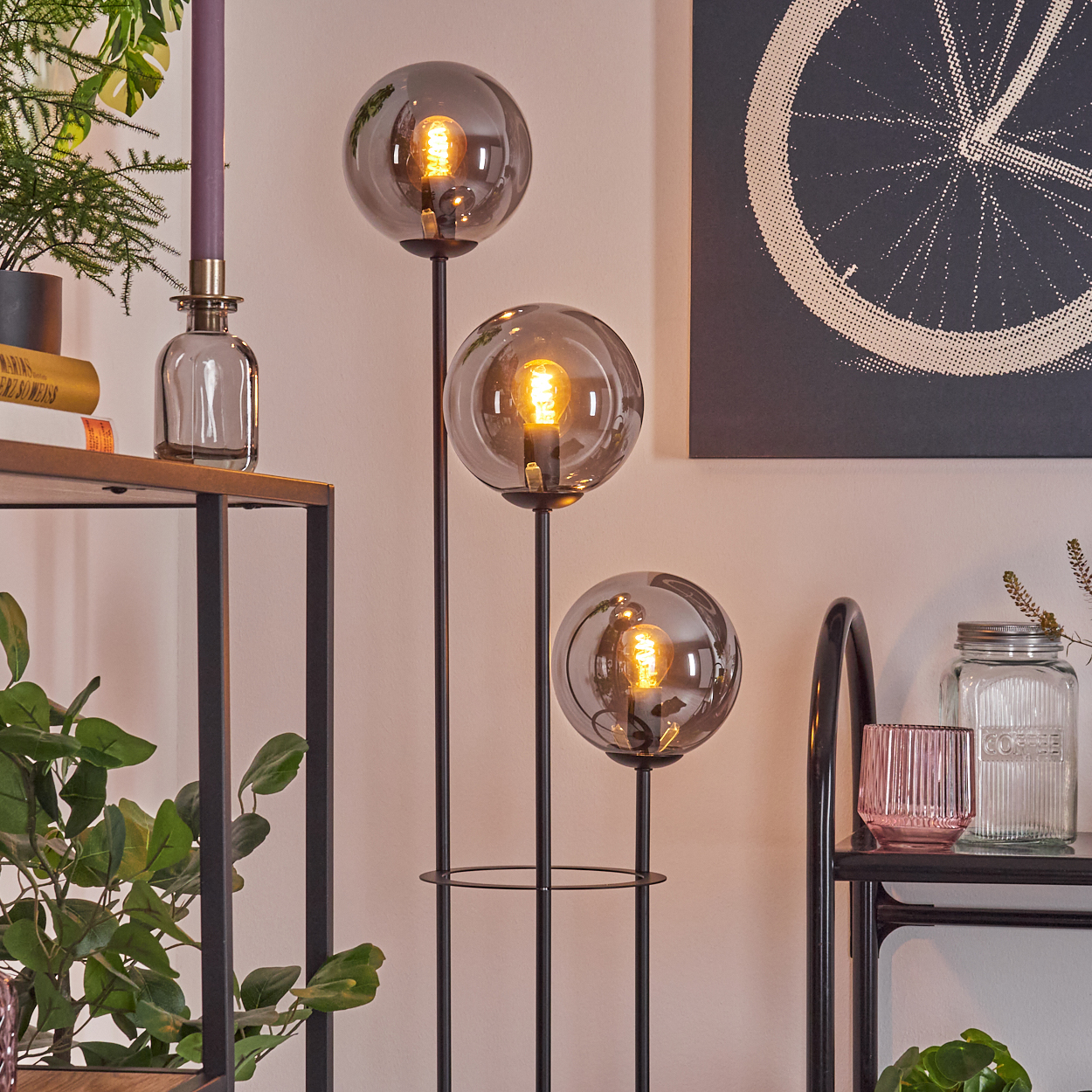Ein modernes Wohnzimmer mit einer dreifach-Glühlampen, einem Fahrradrad-Bild und Dekorationsartikeln auf Regalen, einschließlich Pflanzen und Kerzen.