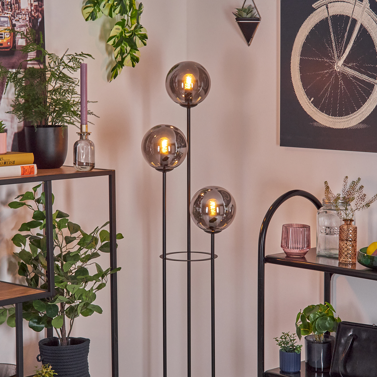 Ein Raum mit einer Stehlampe mit drei kugelförmigen Lichtern. Regale mit Pflanzen und Dekor sind sichtbar.