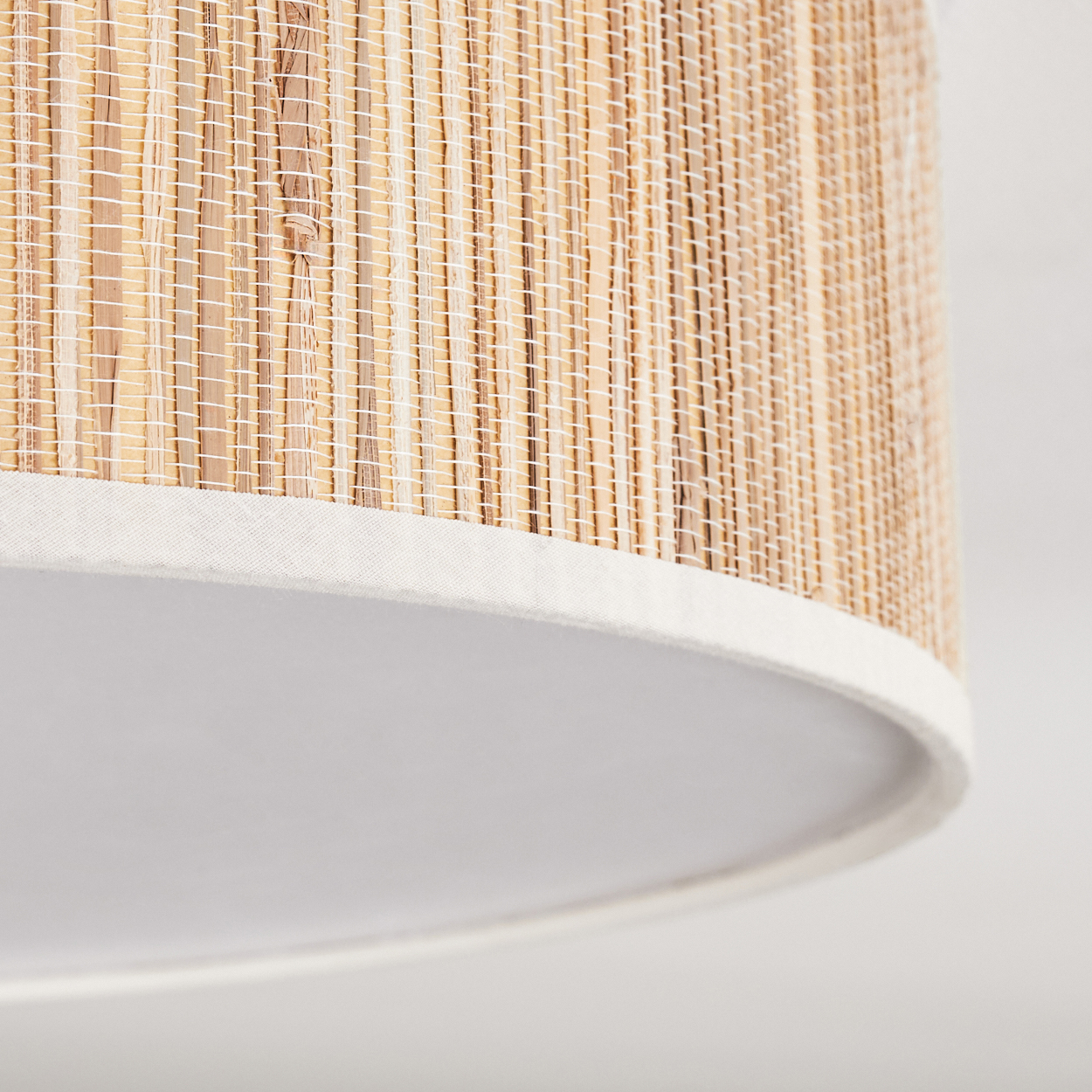 Nahaufnahme eines Lampenschirms. Er hat eine gewebte, beige strukturierte Oberseite, weiße Stoffverkleidung und ein glattes weißes Innere.