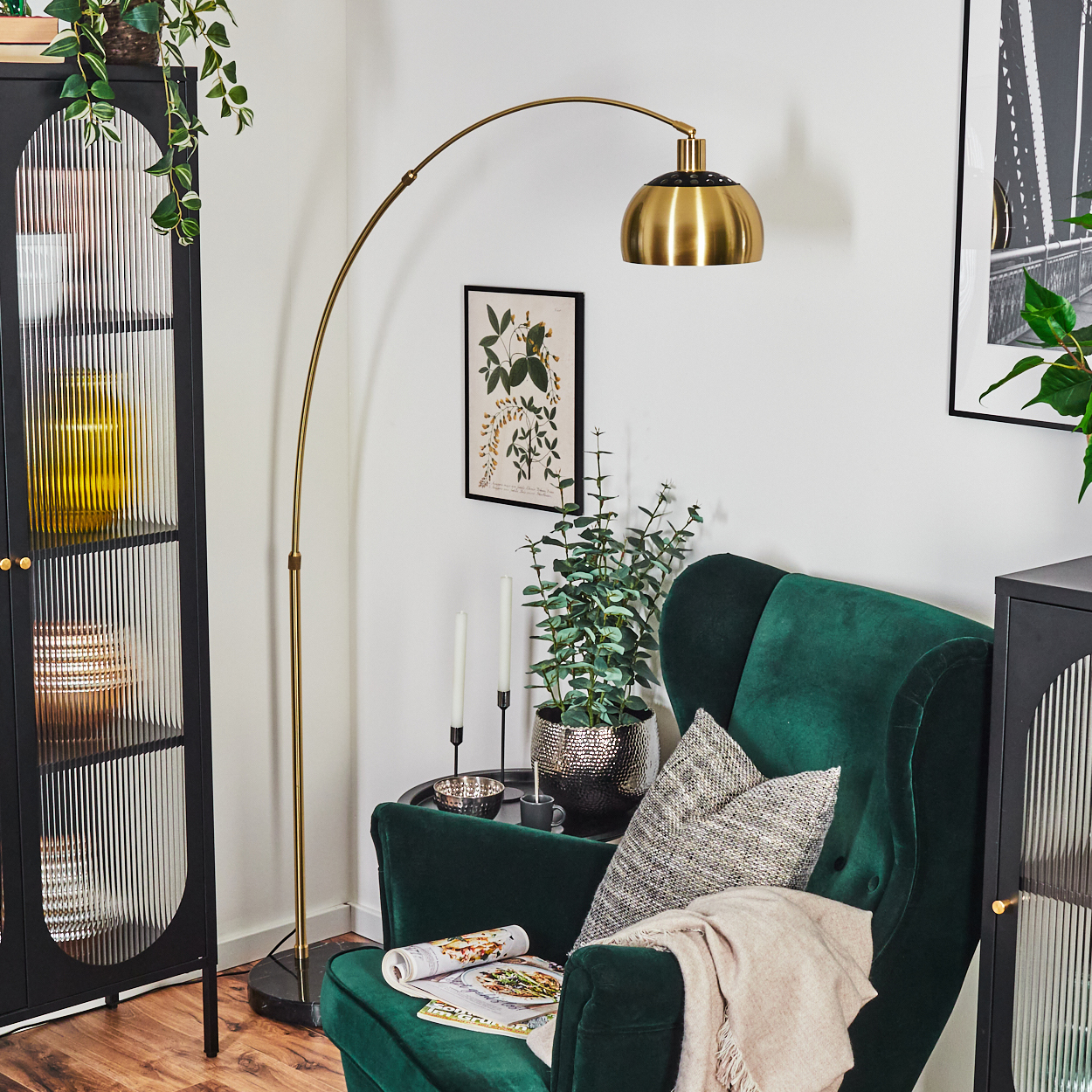Wohnzimmerszene mit grünem Samtsessel, goldener Lampe, schwarzem Schrank, Pflanzen und einem botanischen Druck an der Wand.