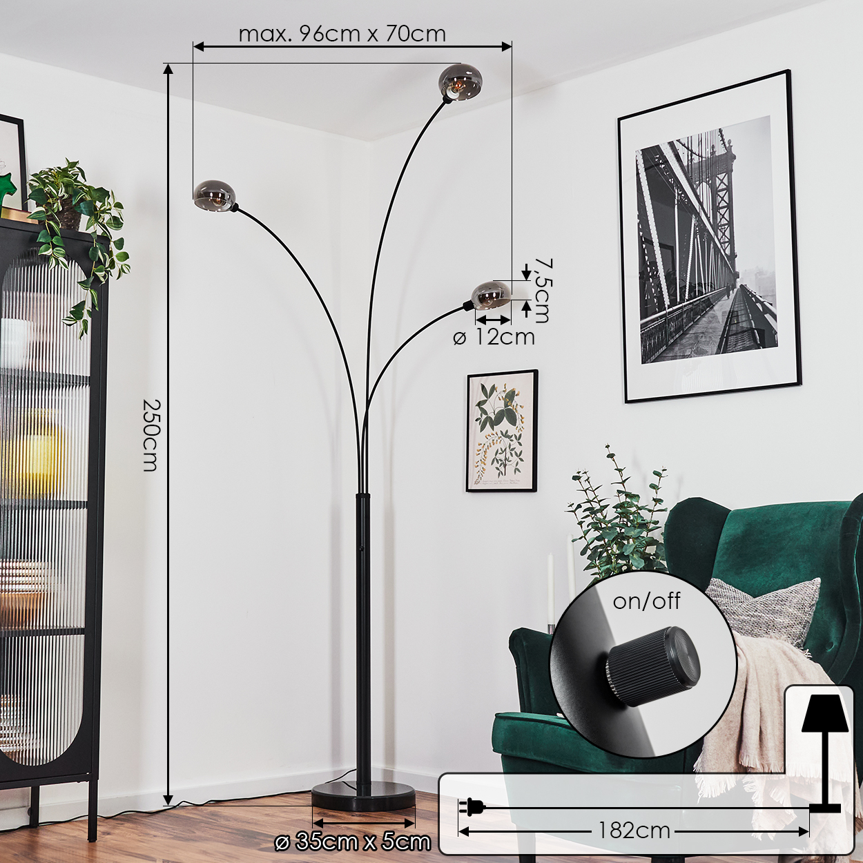 Eine schwarze Stehlampe mit drei Lichtern. Ein grüner Sessel, Schwarz-Weiß-Bilder und ein Schrank im Hintergrund.