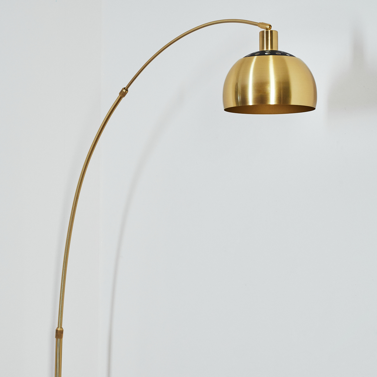 Eine goldene Bogen-Stehlampe vor einer weißen Wand. Die Lampe hat einen kuppelförmigen Kopf und einen gebogenen Stiel.
