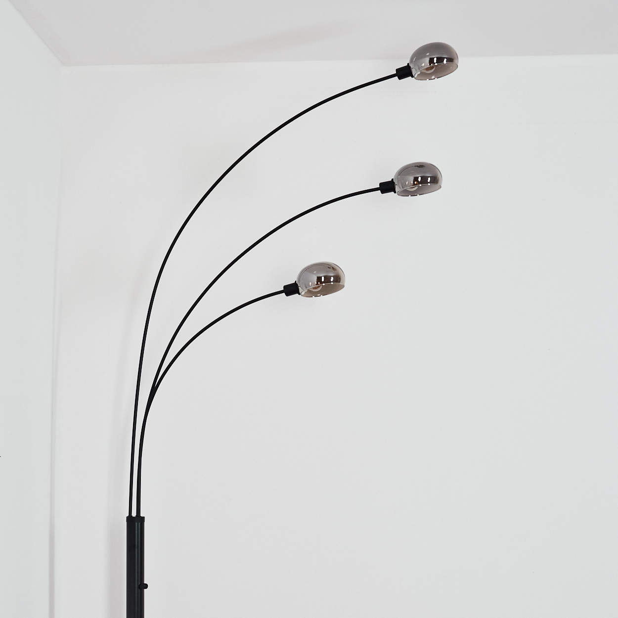 Eine moderne schwarze Stehlampe mit drei gebogenen Armen, die jeweils ein silbernes, kugelförmiges Licht halten, vor einer weißen Wand.