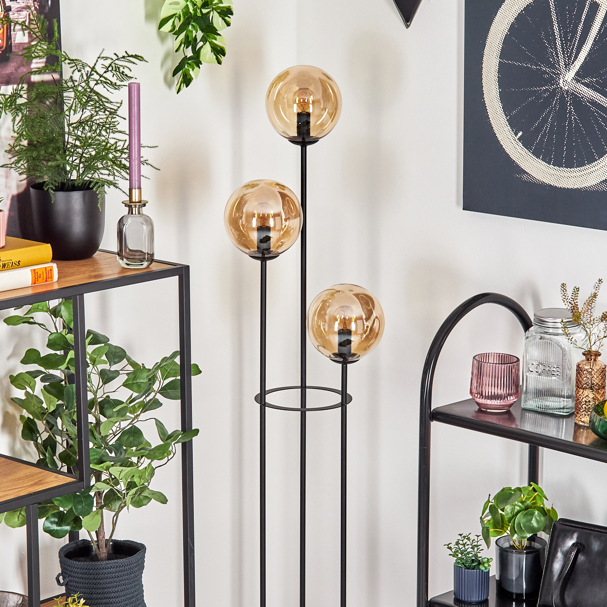 Ein modernes Zimmer mit Stehlampe, drei Kugelleuchten, Pflanzen, Regalen und Dekorationsartikeln. Die Farbpalette ist neutral.