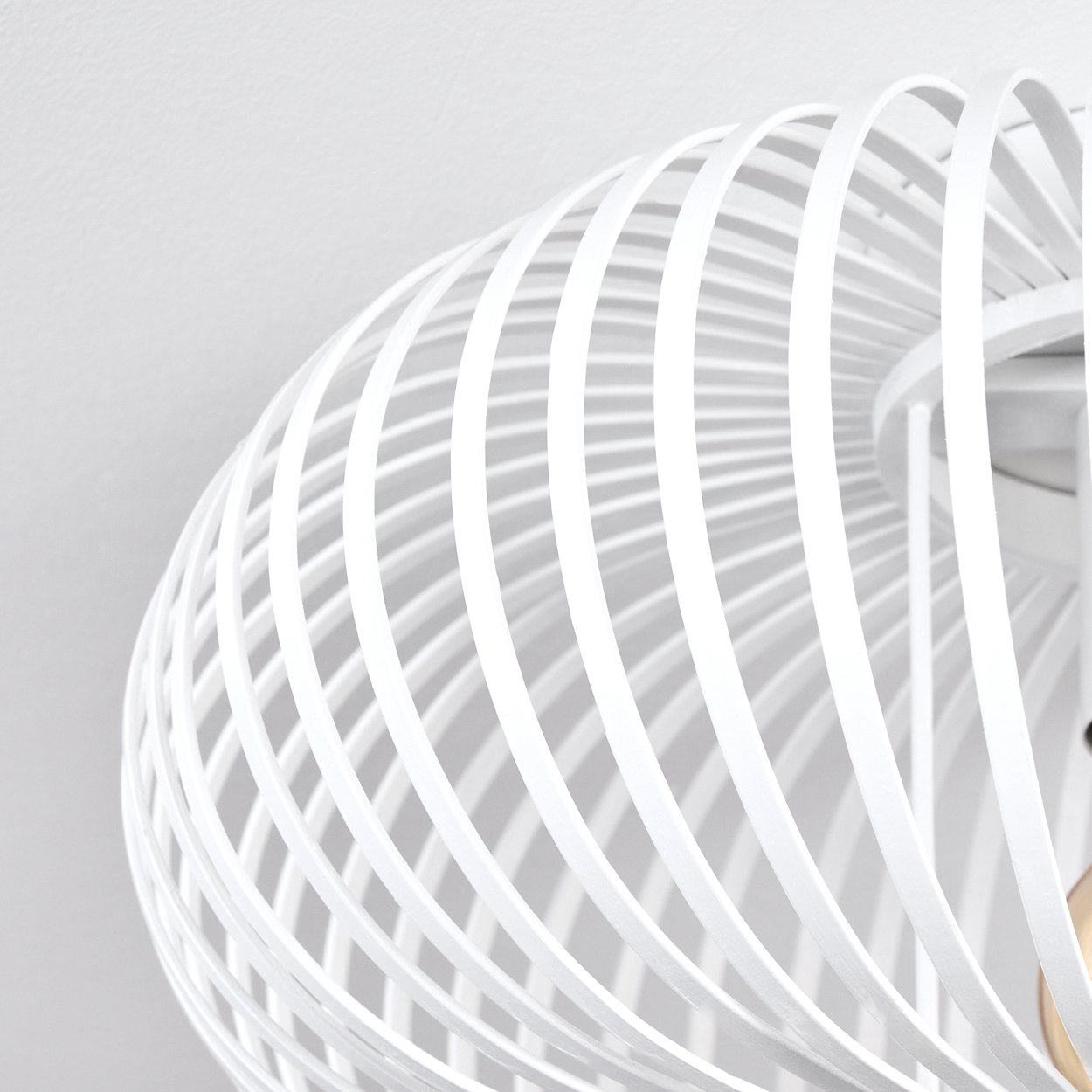 Nahaufnahme einer weißen, spiralförmigen Leuchte vor weißem Hintergrund. Das Design hat gebogene, parallele Stäbe.