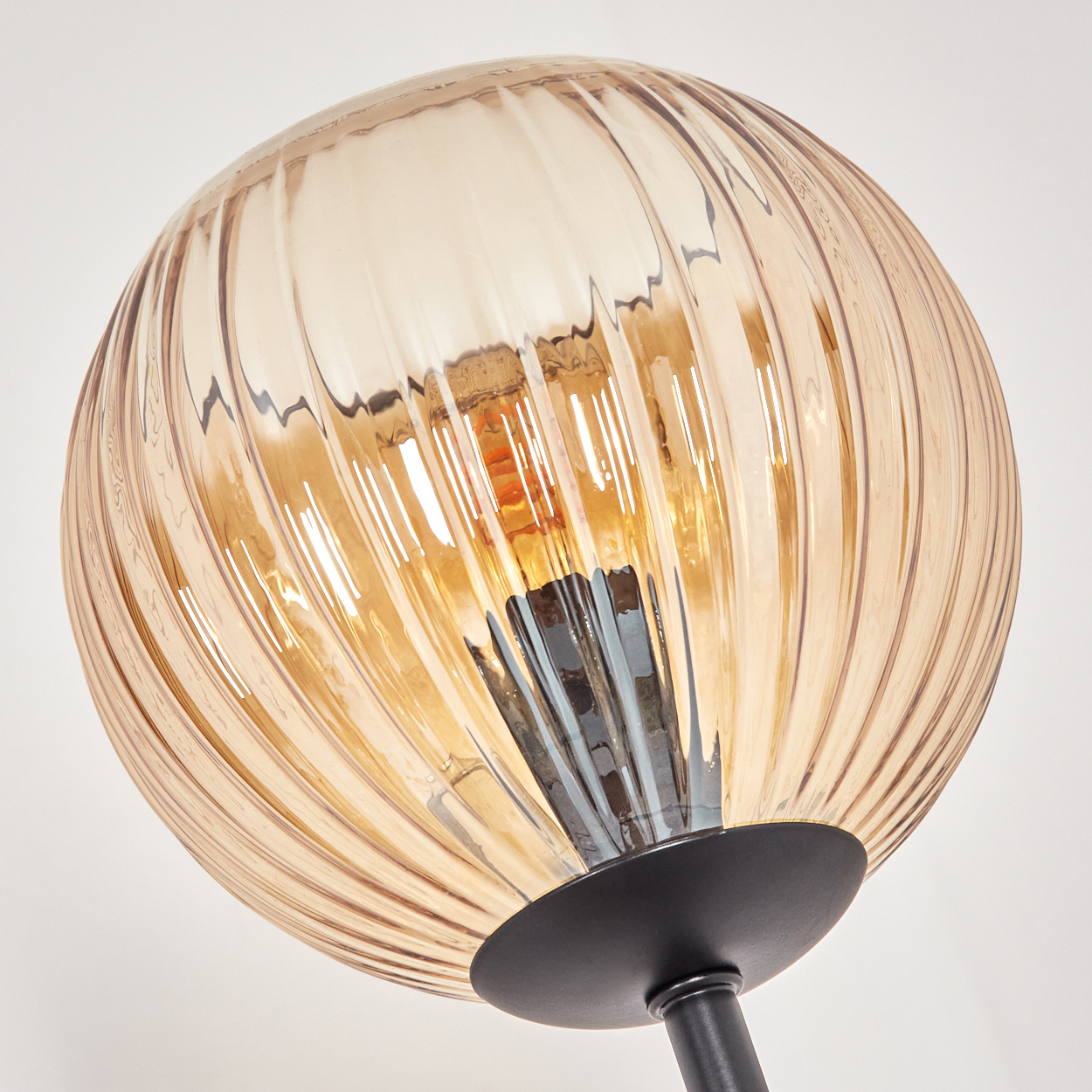 Nahaufnahme einer dekorativen Lampe. Sie hat einen runden, gerippten, bernsteinfarbenen Glasschirm mit schwarzem Sockel und Stiel. Weißer Hintergrund.