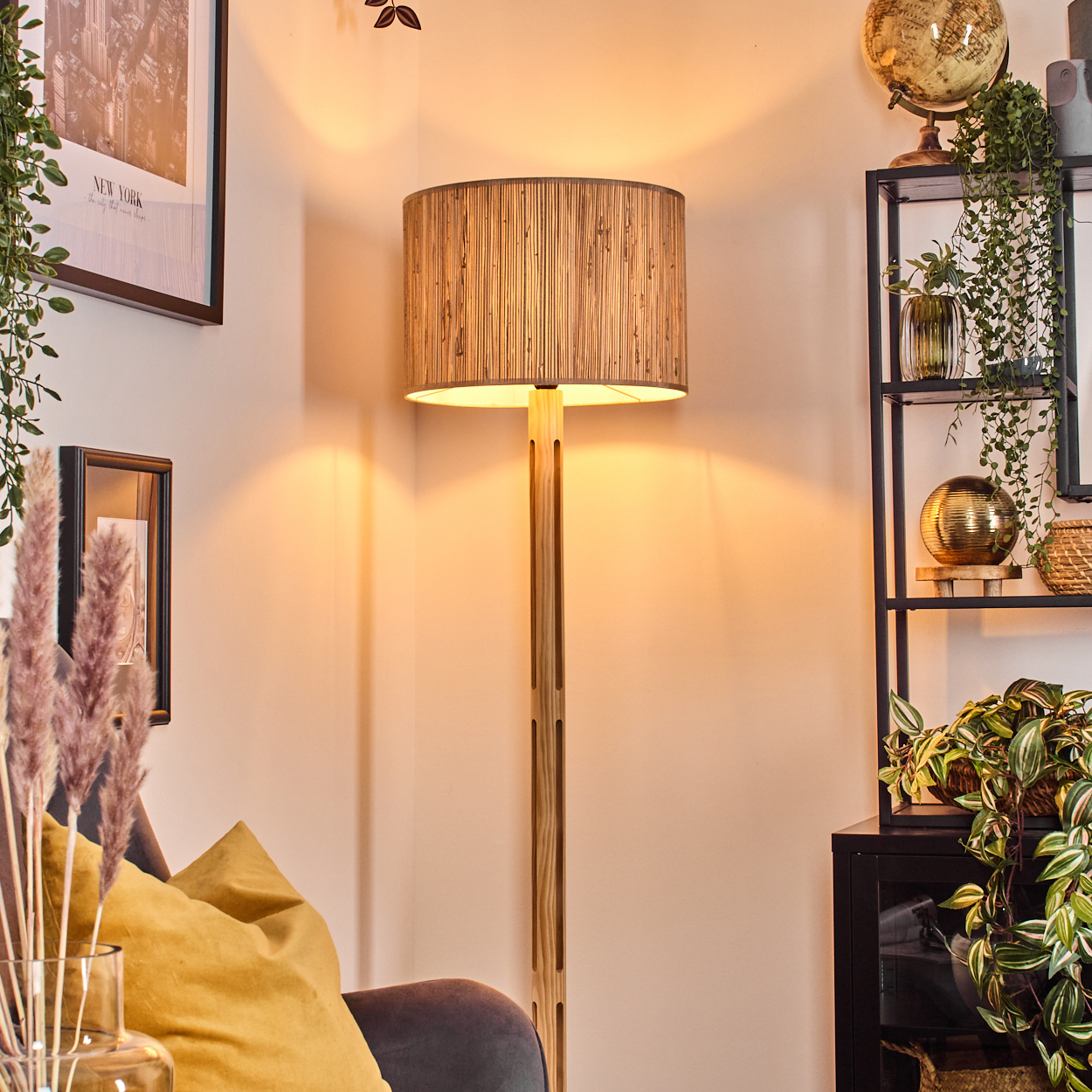Eine beleuchtete Stehlampe aus Holz steht in einem Raum. Pflanzen, Bilder und ein Globus sind ebenfalls zu sehen.