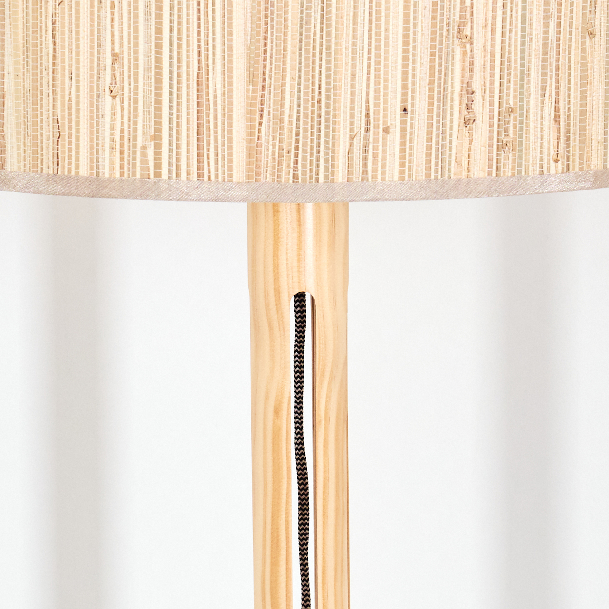 Nahaufnahme einer Lampe. Der Lampenschirm ist gewebt und beige, der Holzkörper hellbraun und das Kabel schwarz.