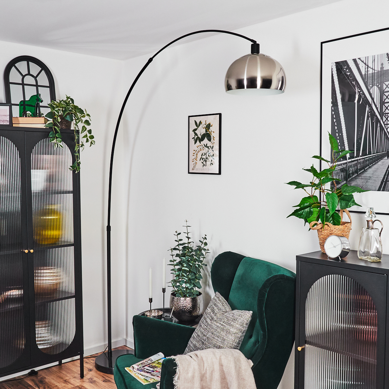 Wohnzimmer mit grünem Sessel, schwarzen Schränken, Bogenlampe und Brückenbild. Pflanzen und Dekoration vorhanden.